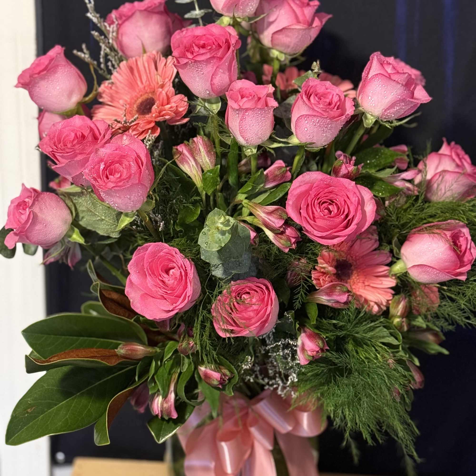 Pink roses and gerbera daisies in a bouquet with a pink ribbon