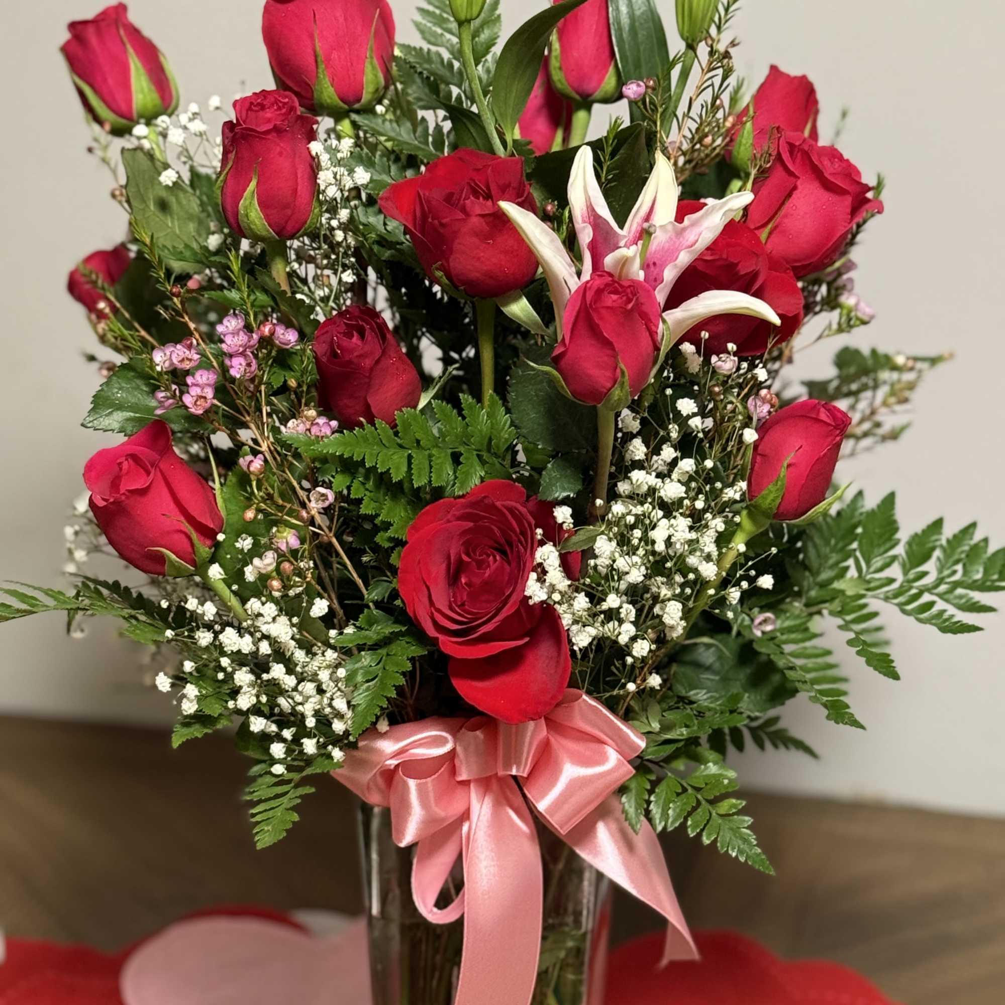 Red roses and lilies arranged in a clear vase with a pink ribbon