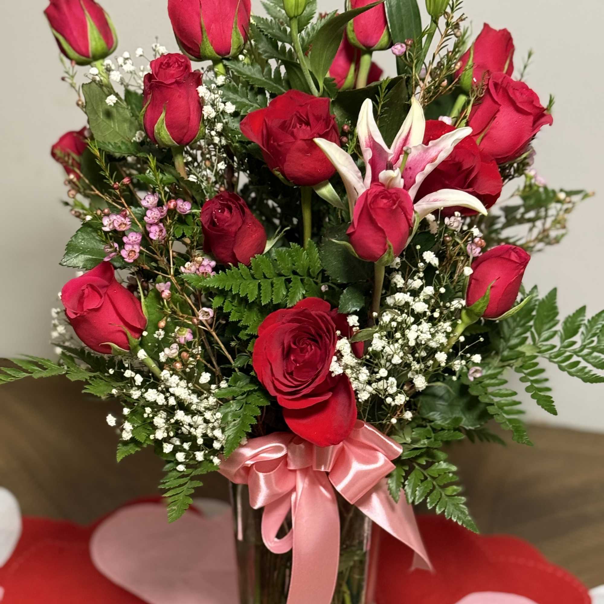 Red roses and a white lily in a glass vase with a pink ribbon