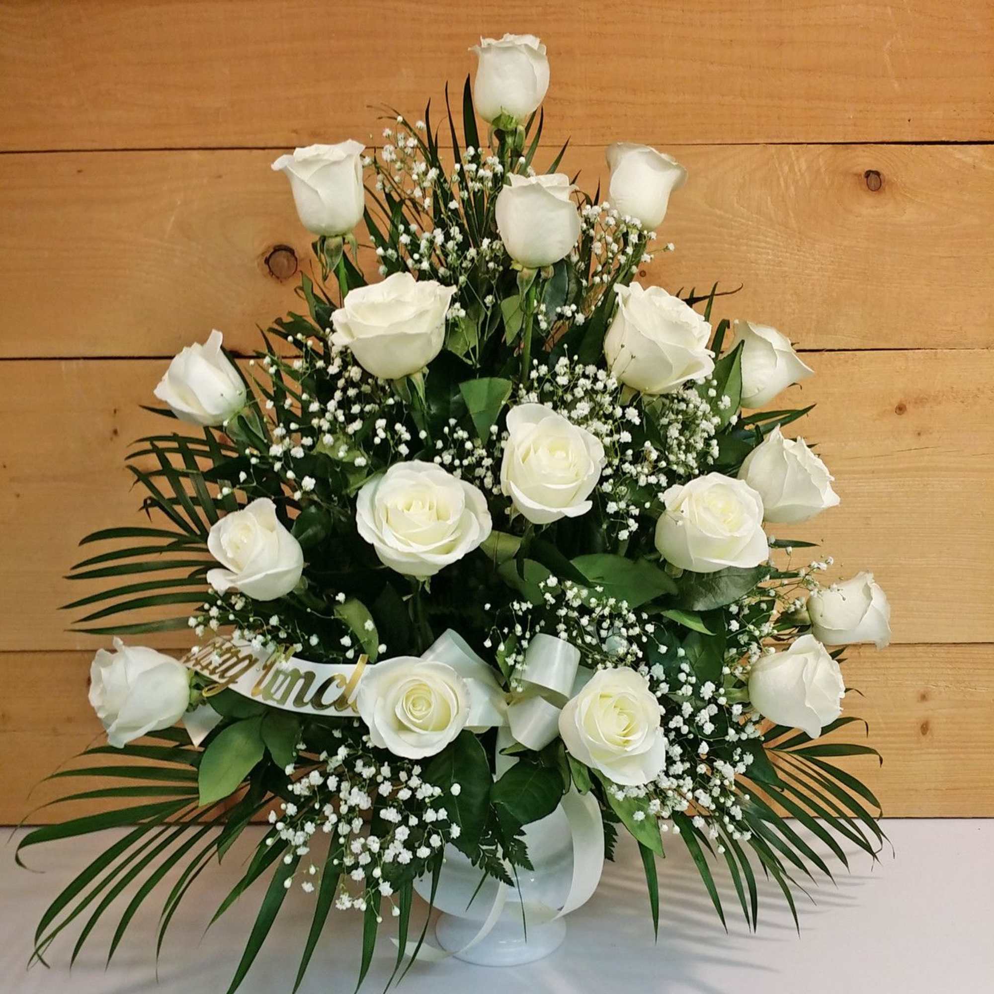 White roses arranged in a vase with baby's breath and palm fronds