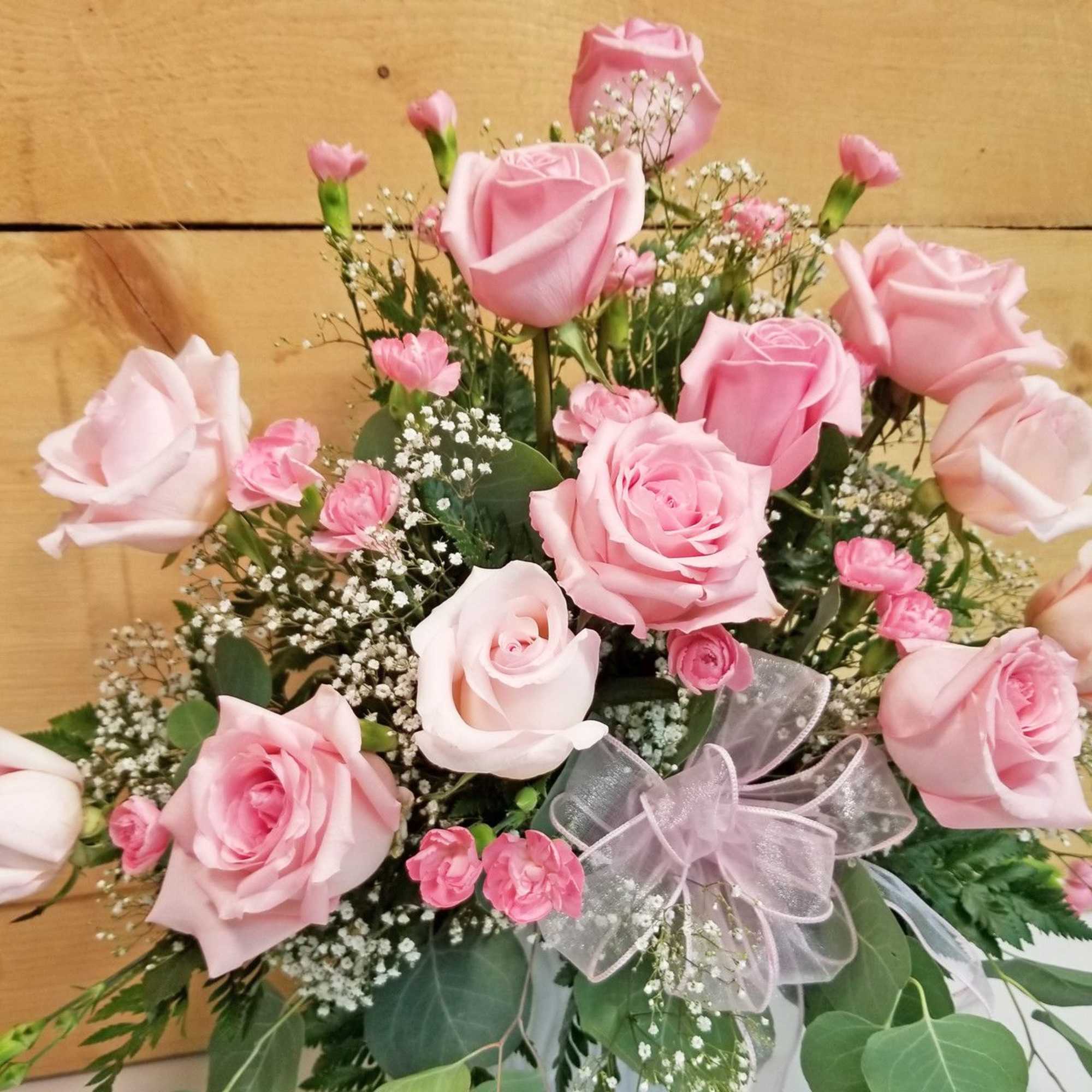 Pink roses and small pink carnations in a bouquet with a sheer ribbon