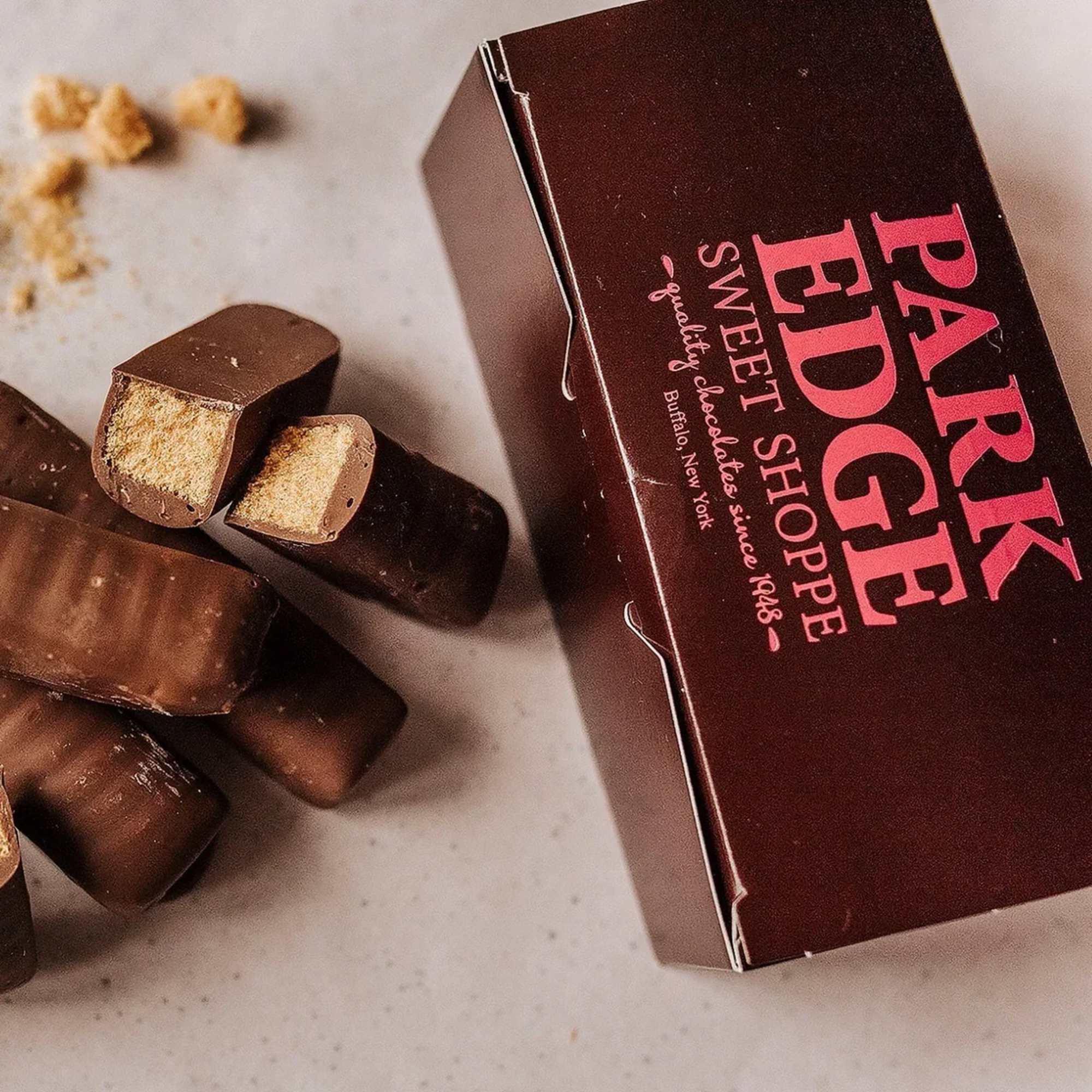 Box of chocolate-covered candy bars with several pieces stacked and one cut open on a light surface