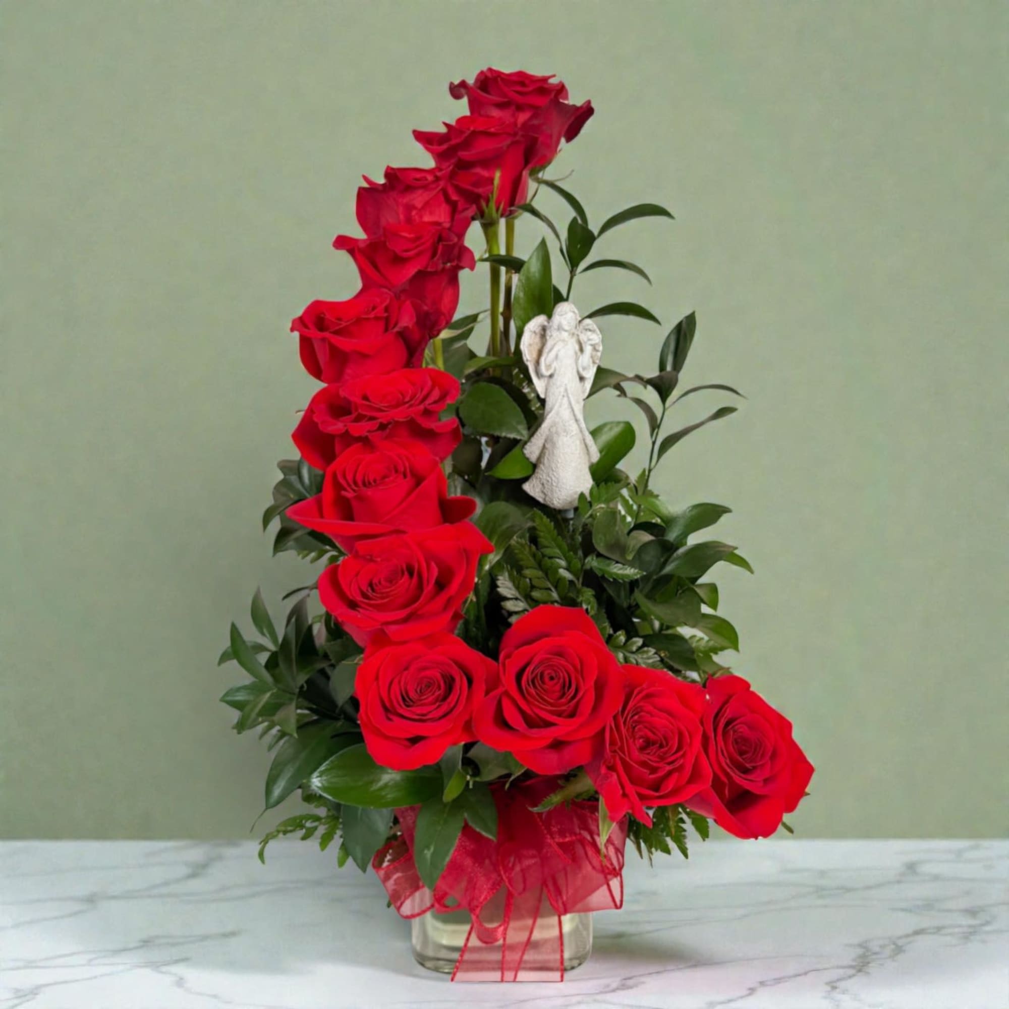 Red roses arranged in a clear glass vase with a small angel figurine