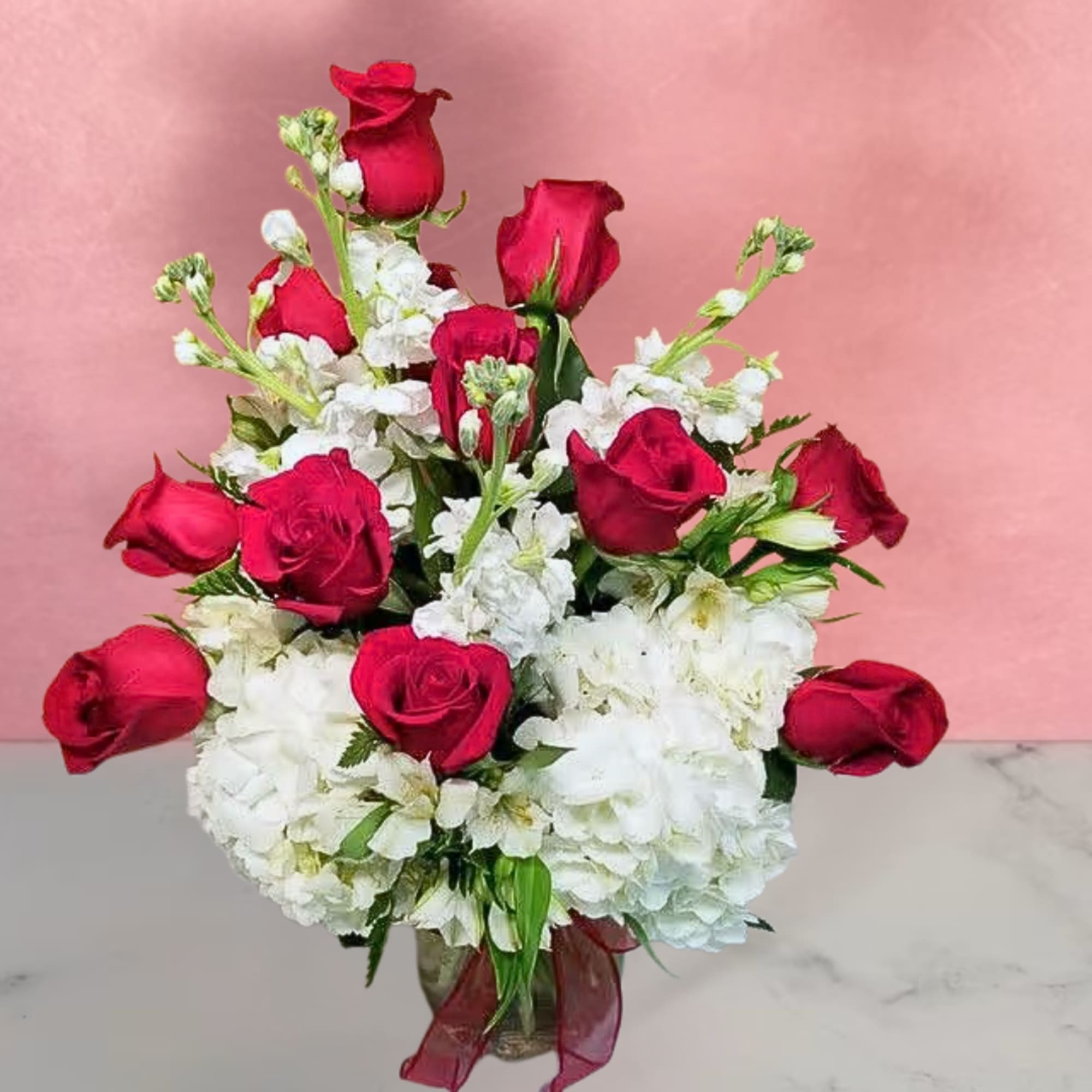 Red roses and white flowers arranged in a glass vase with a red ribbon