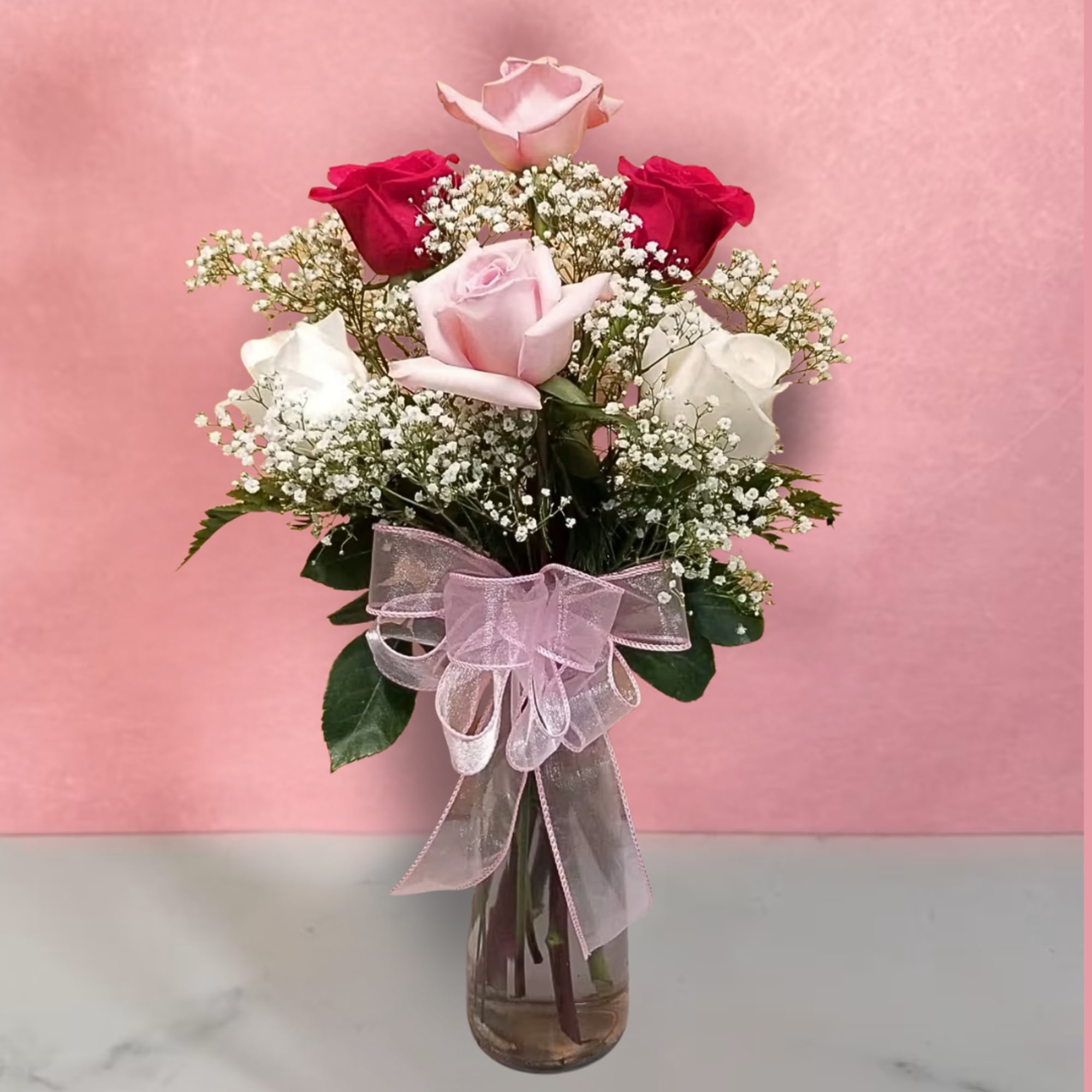 Pink and red roses in a glass vase with a pink ribbon