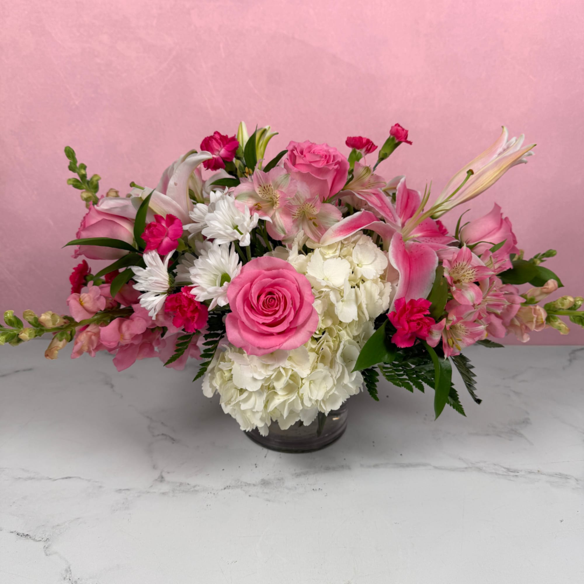 Low pink and white arrangement with roses, lilies, hydrangeas, and daisies in a glass vase