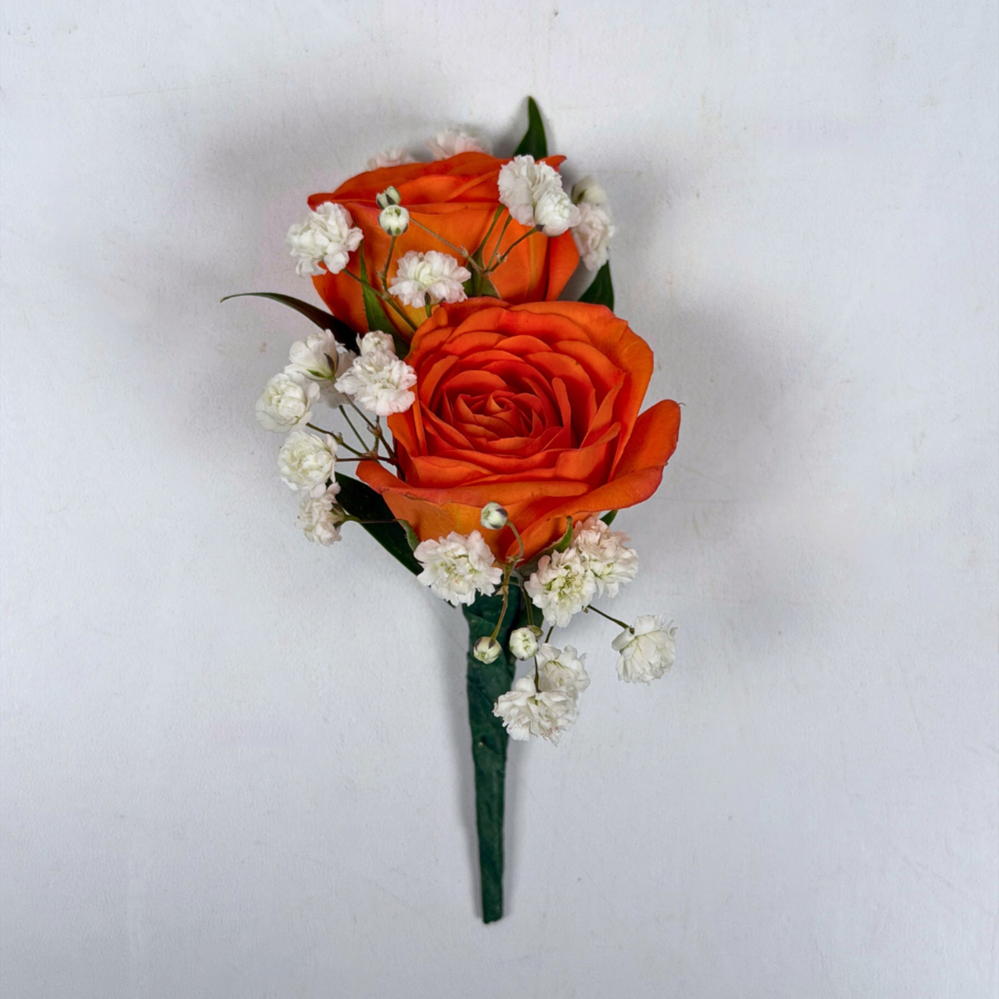 Two vivid orange rose blooms make this boutonniere a bright, celebratory accent