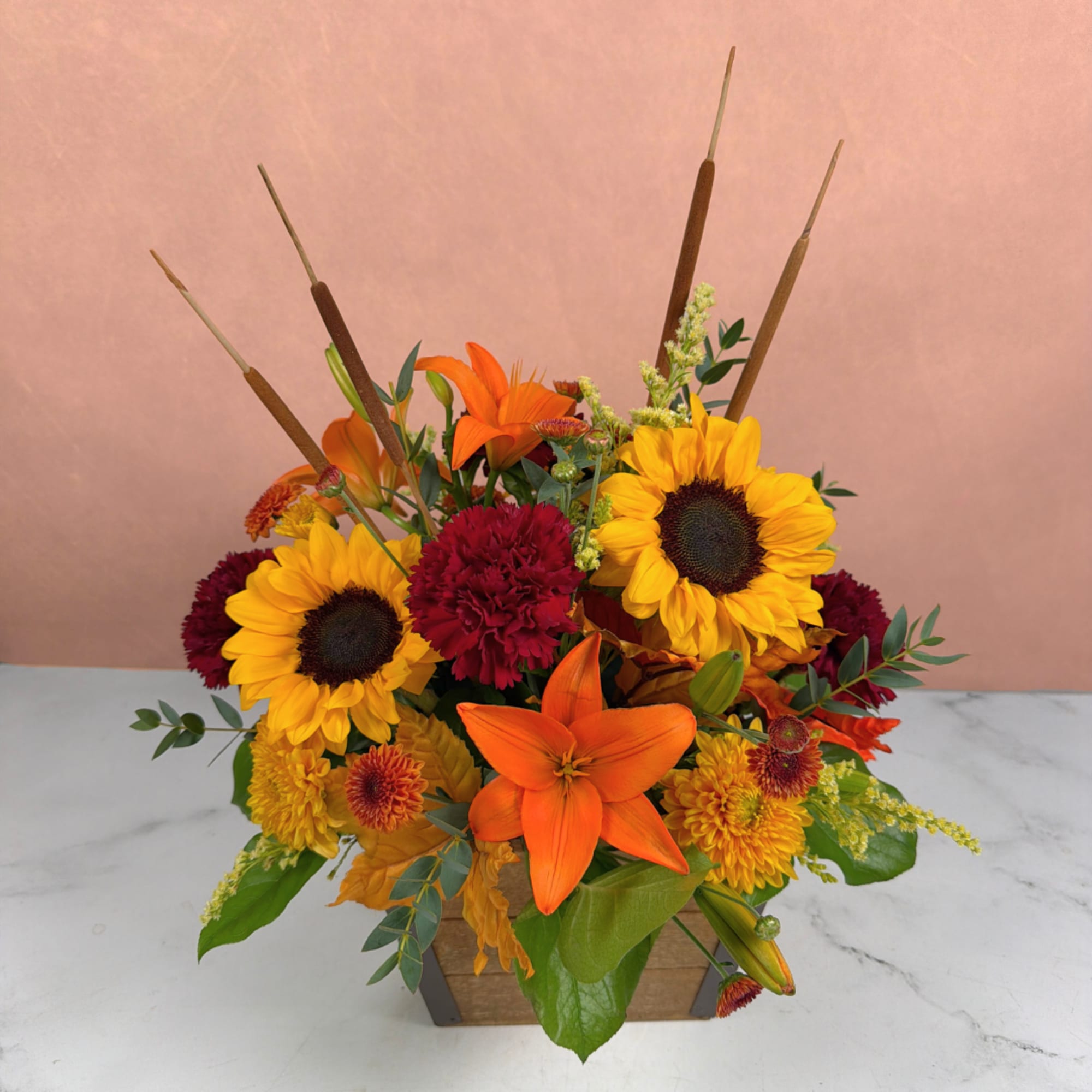 Orange lilies and sunflowers in a wooden container with cattails