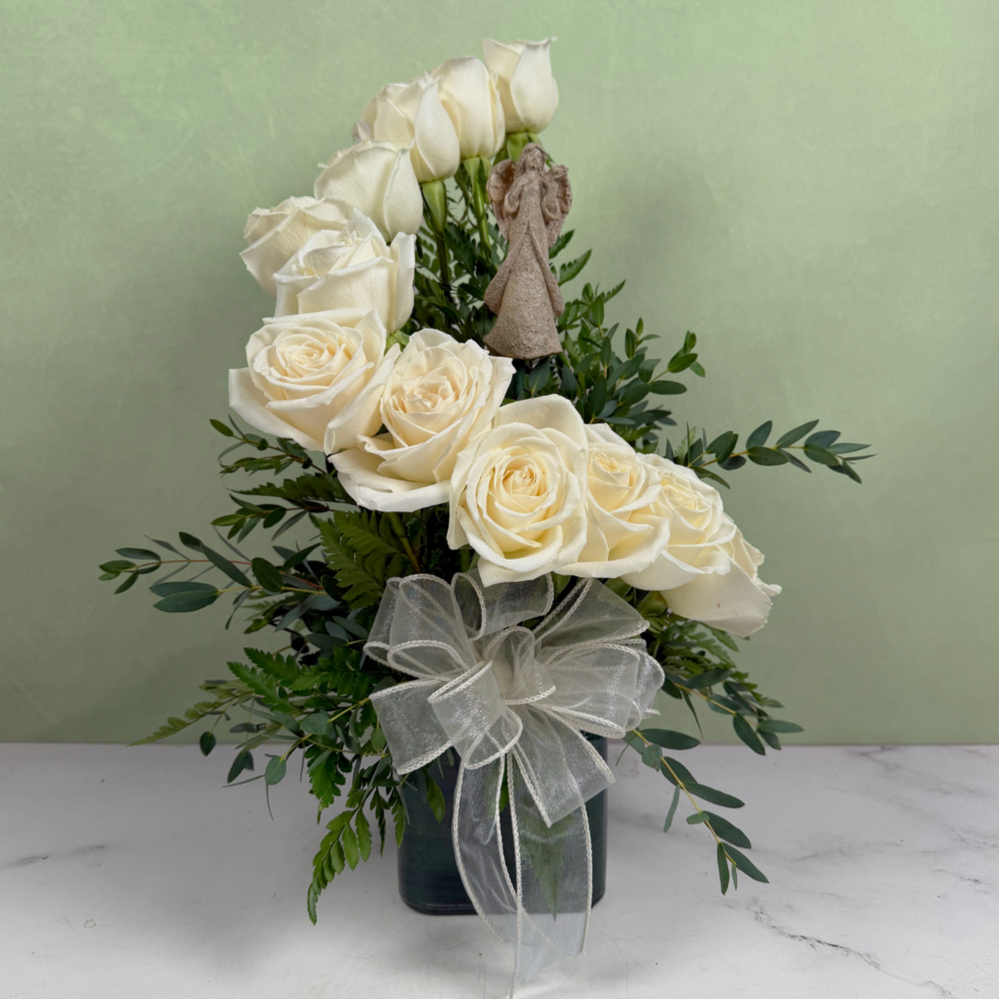 White roses arranged in a dark vase with a sheer bow and angel figurine