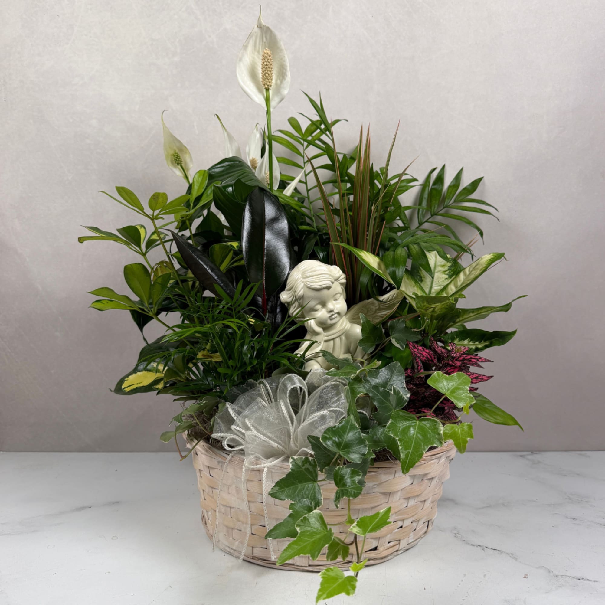 Mixed potted plants in a woven basket with a small angel figurine