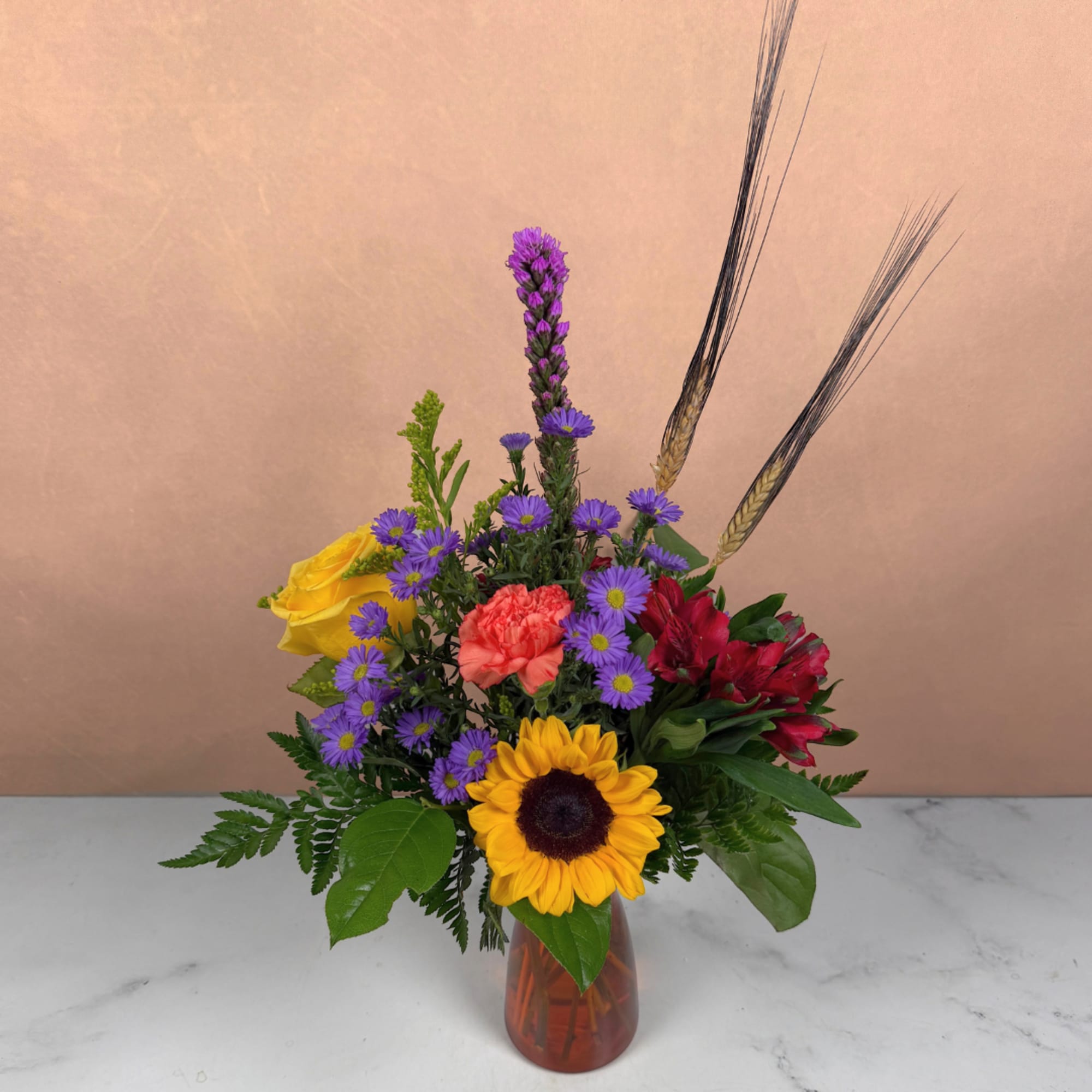 Mixed bouquet in a glass vase with a sunflower, roses, and purple daisies