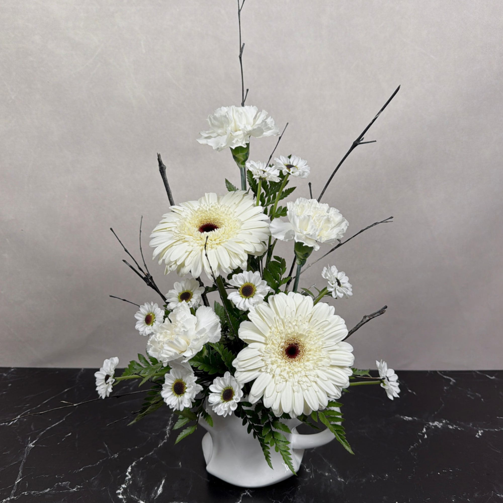 White gerbera daisies and carnations arranged in a white pitcher vase