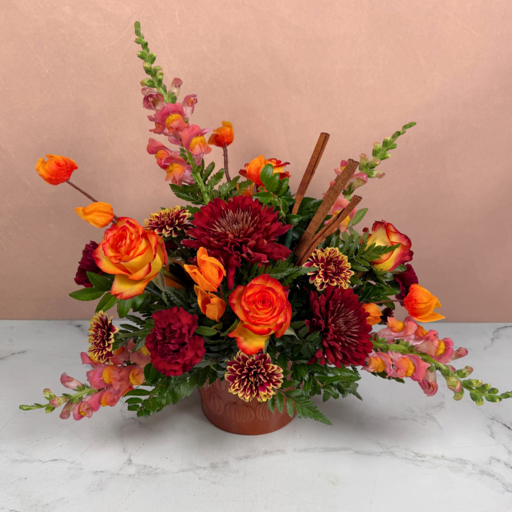 Mixed orange, red, and pink flowers arranged in a low ceramic vase