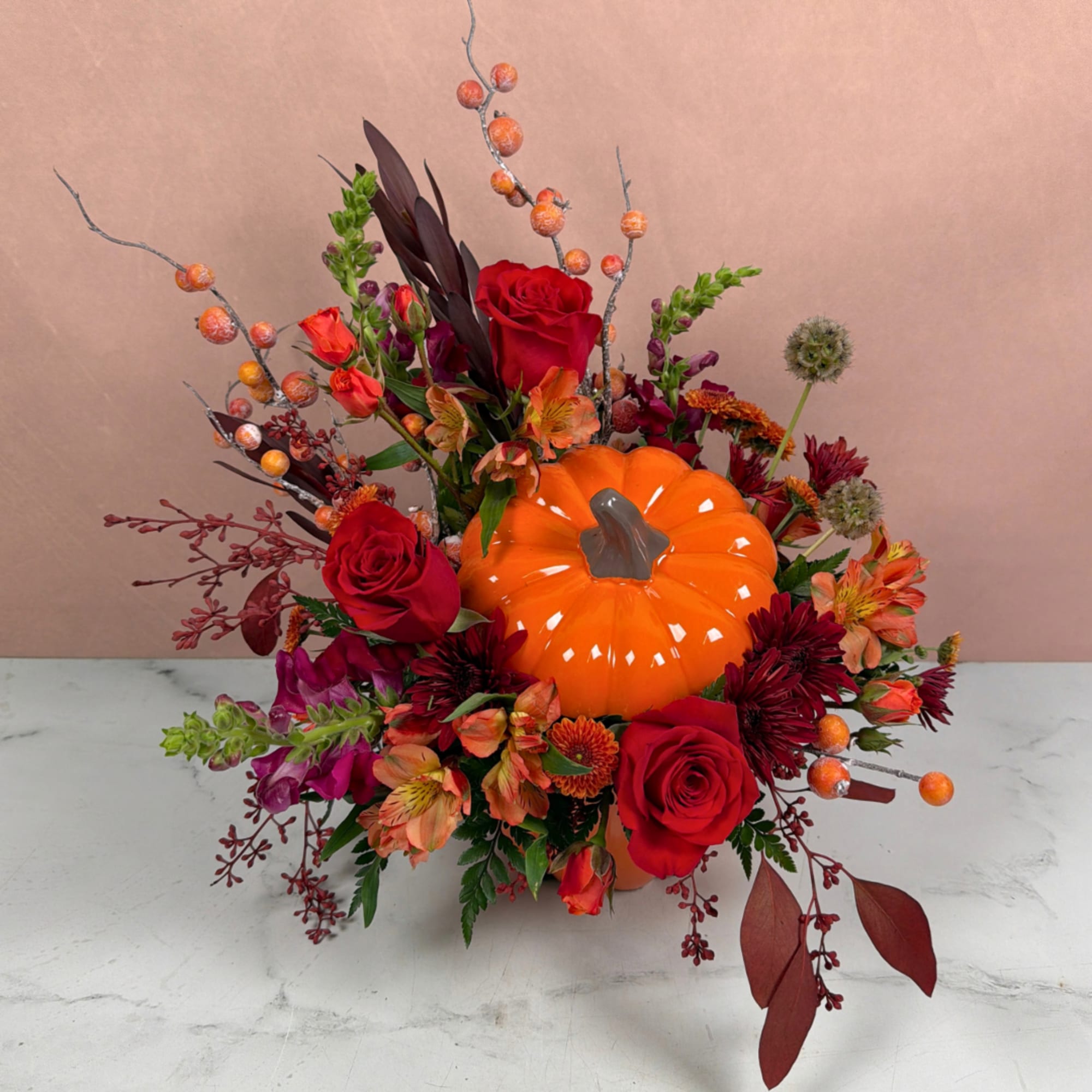 Autumn floral arrangement with red roses and an orange pumpkin centerpiece