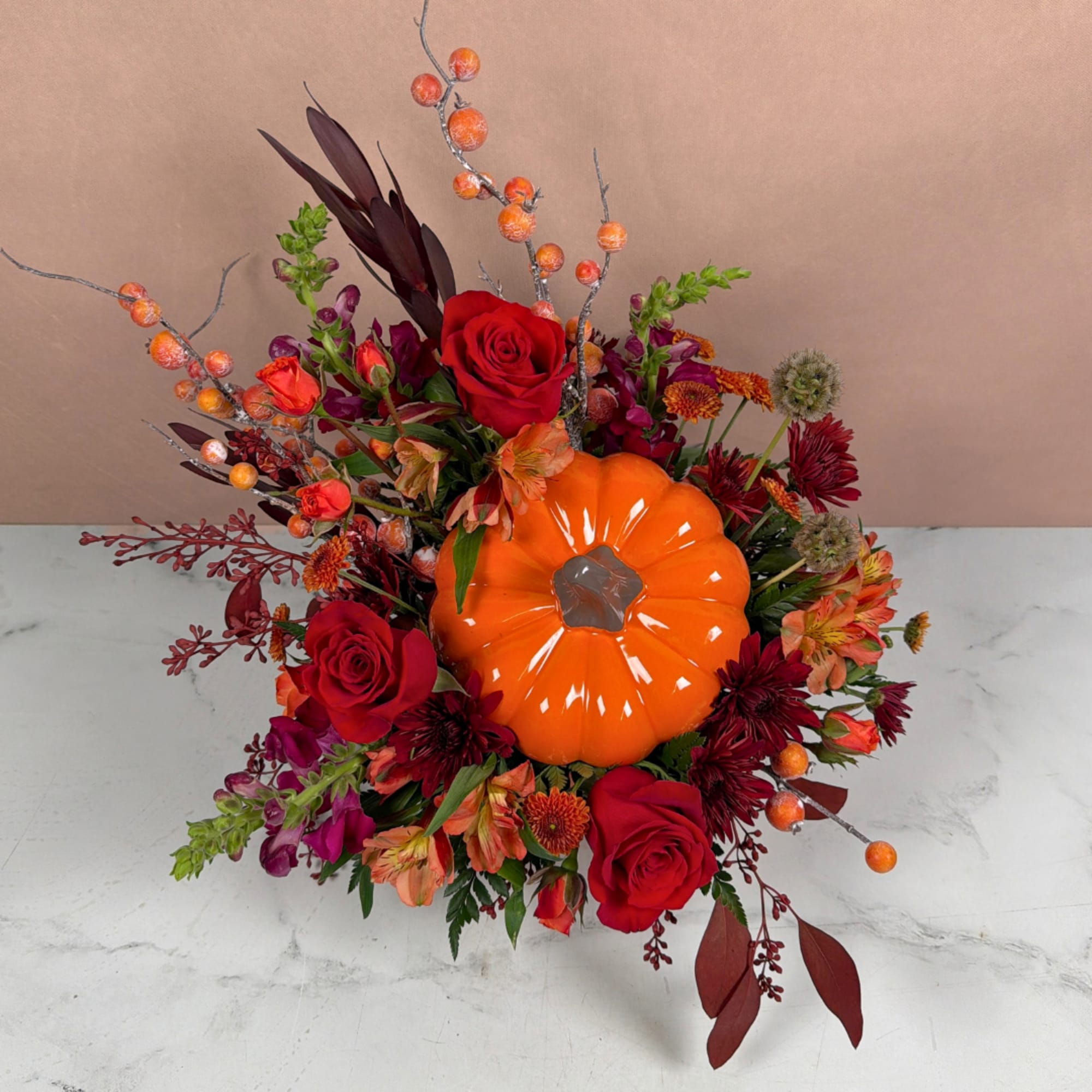 Fall floral arrangement with roses, chrysanthemums, and a bright orange pumpkin centerpiece
