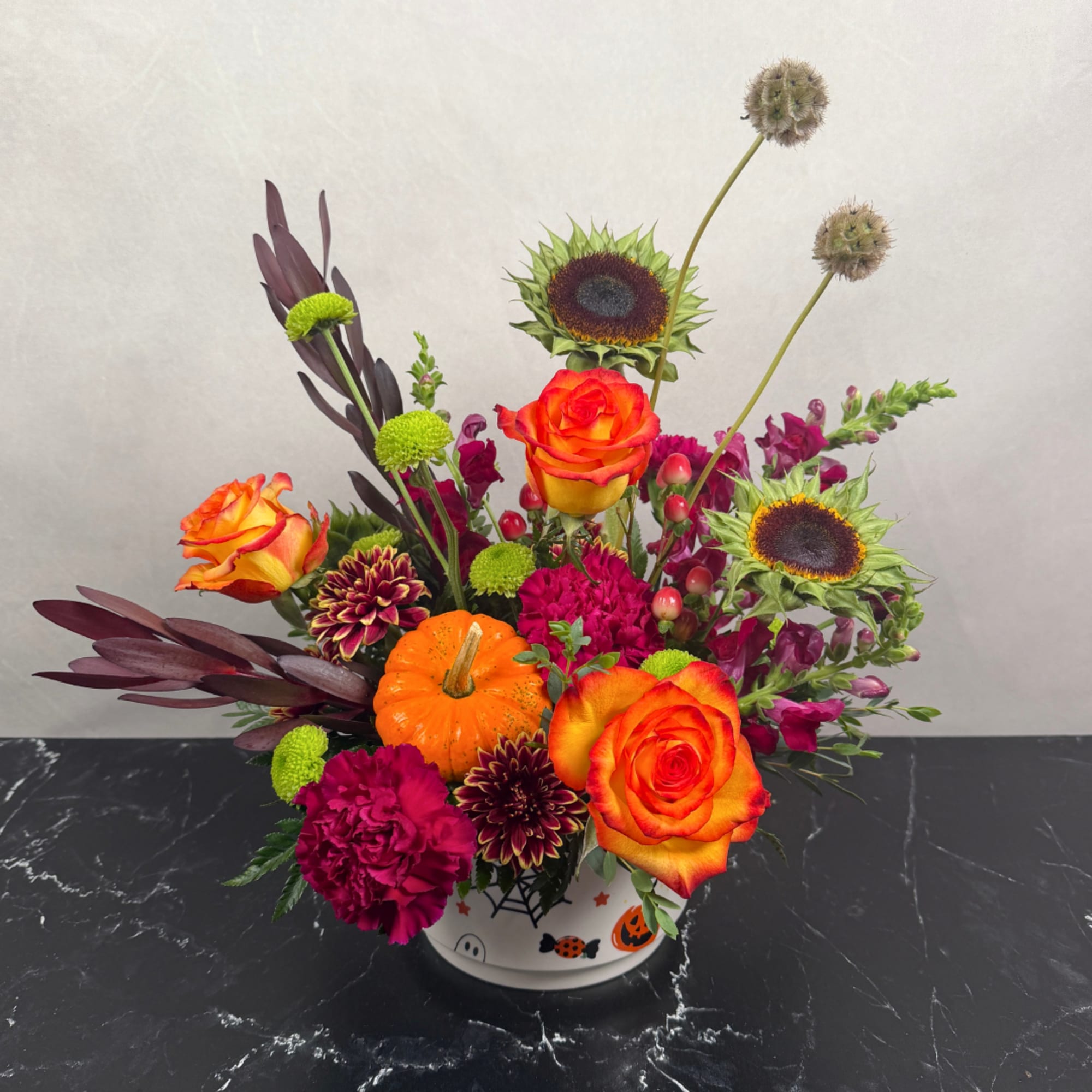 Colorful floral arrangement in a Halloween-themed container with roses and sunflowers