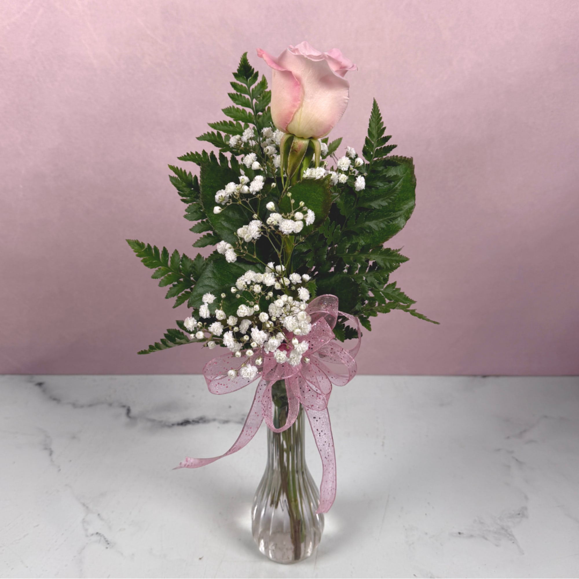 Pink rose in a clear glass vase with baby's breath and a pink ribbon