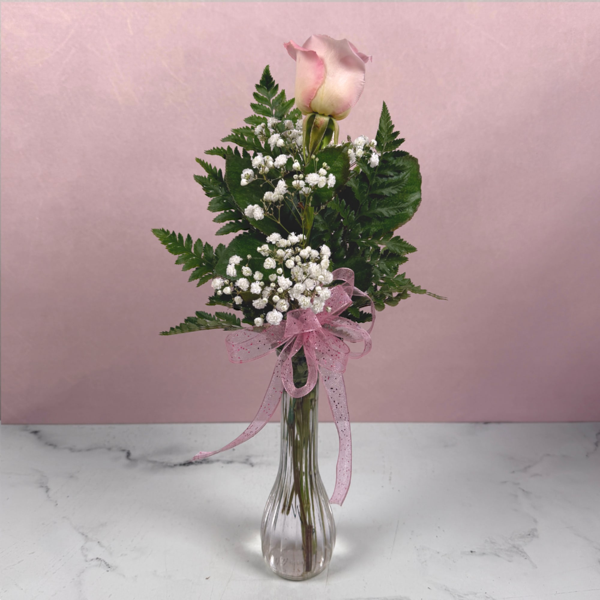 Single pink rose in a clear glass vase with baby's breath and a pink ribbon