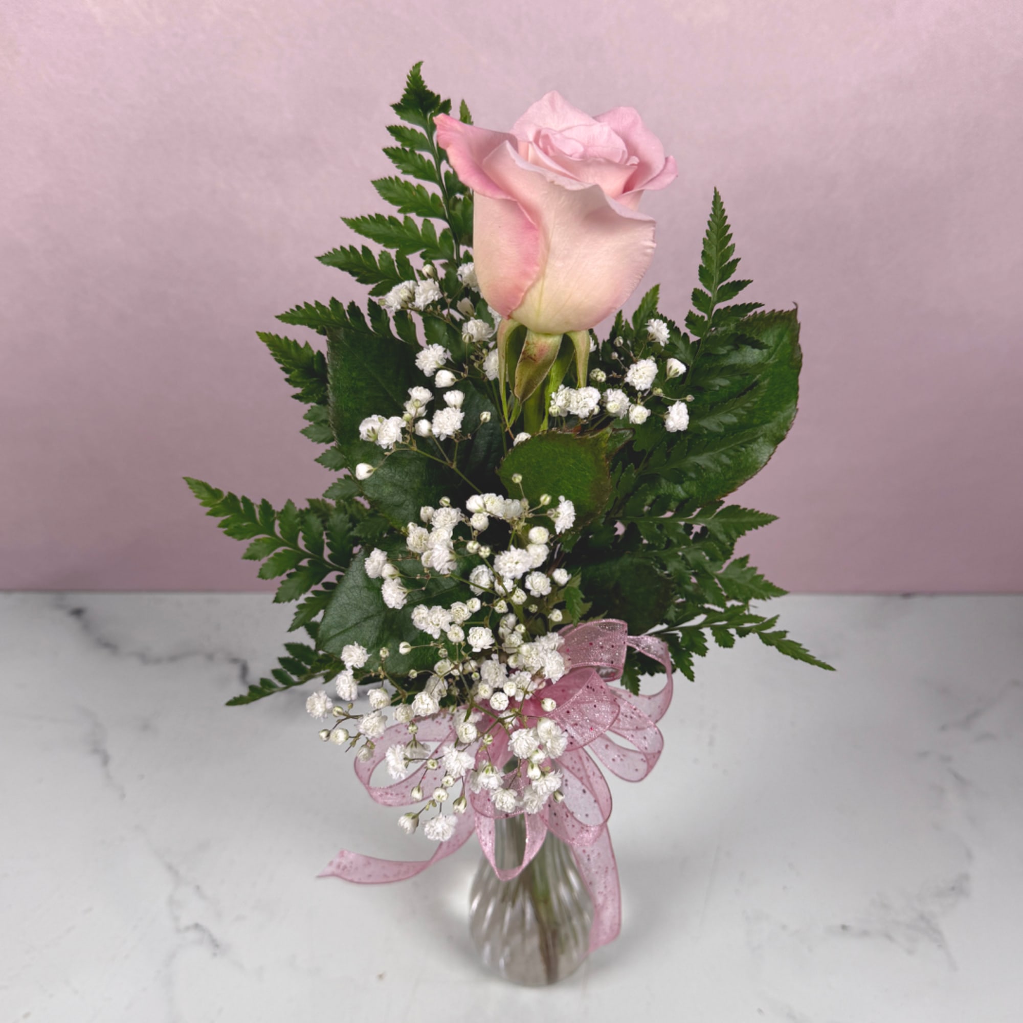 Pink rose arrangement with baby's breath in a clear vase and pink ribbon