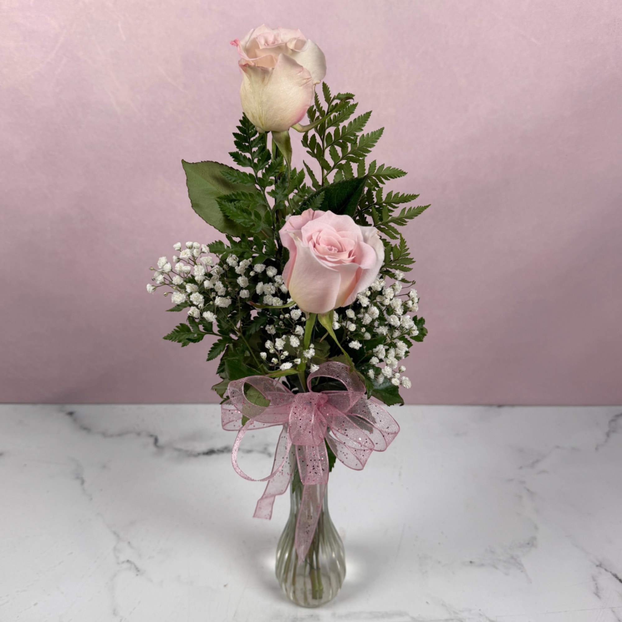 Pink roses with baby's breath in a clear glass vase tied with a pink ribbon