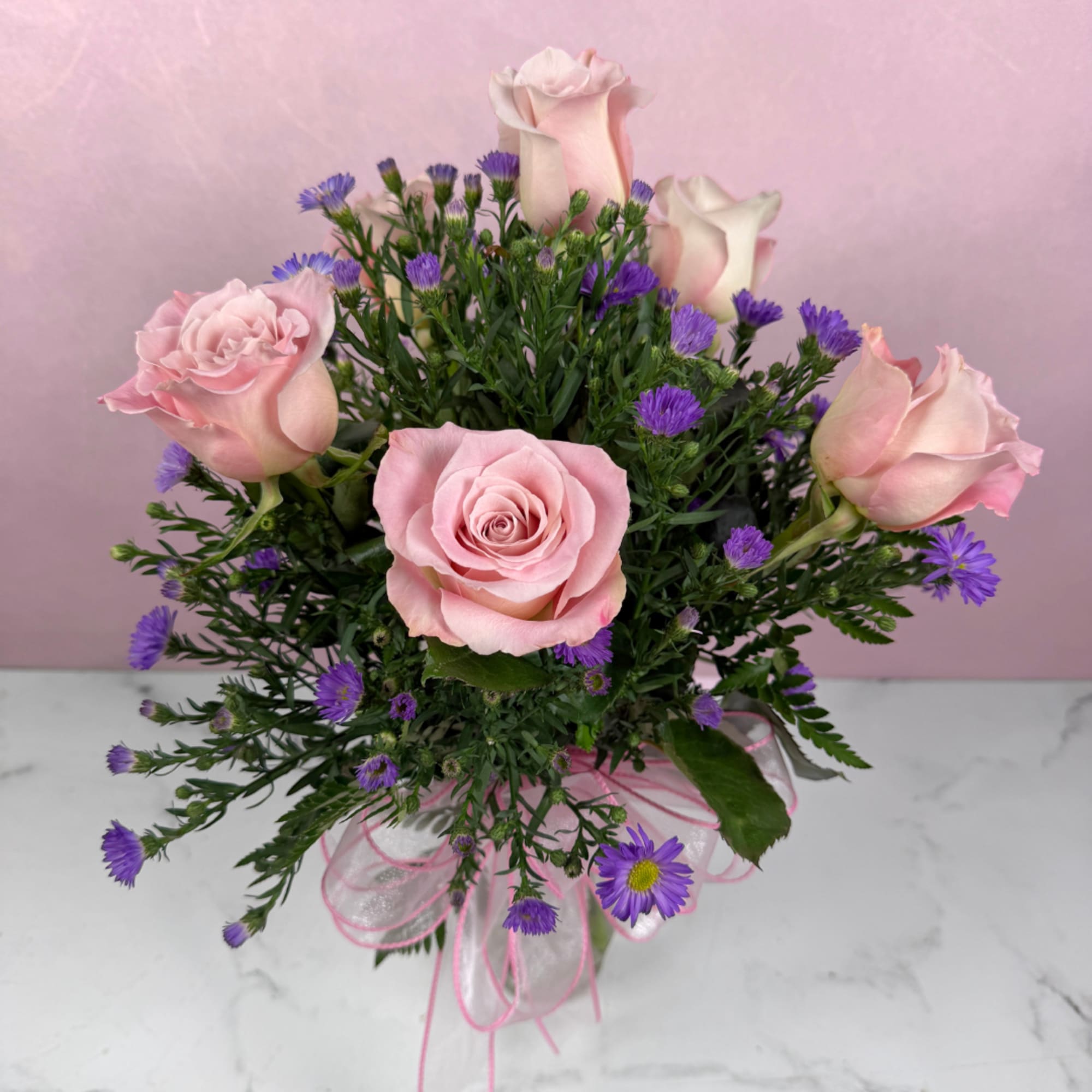 Pink roses and purple daisies in a clear vase with a pink ribbon