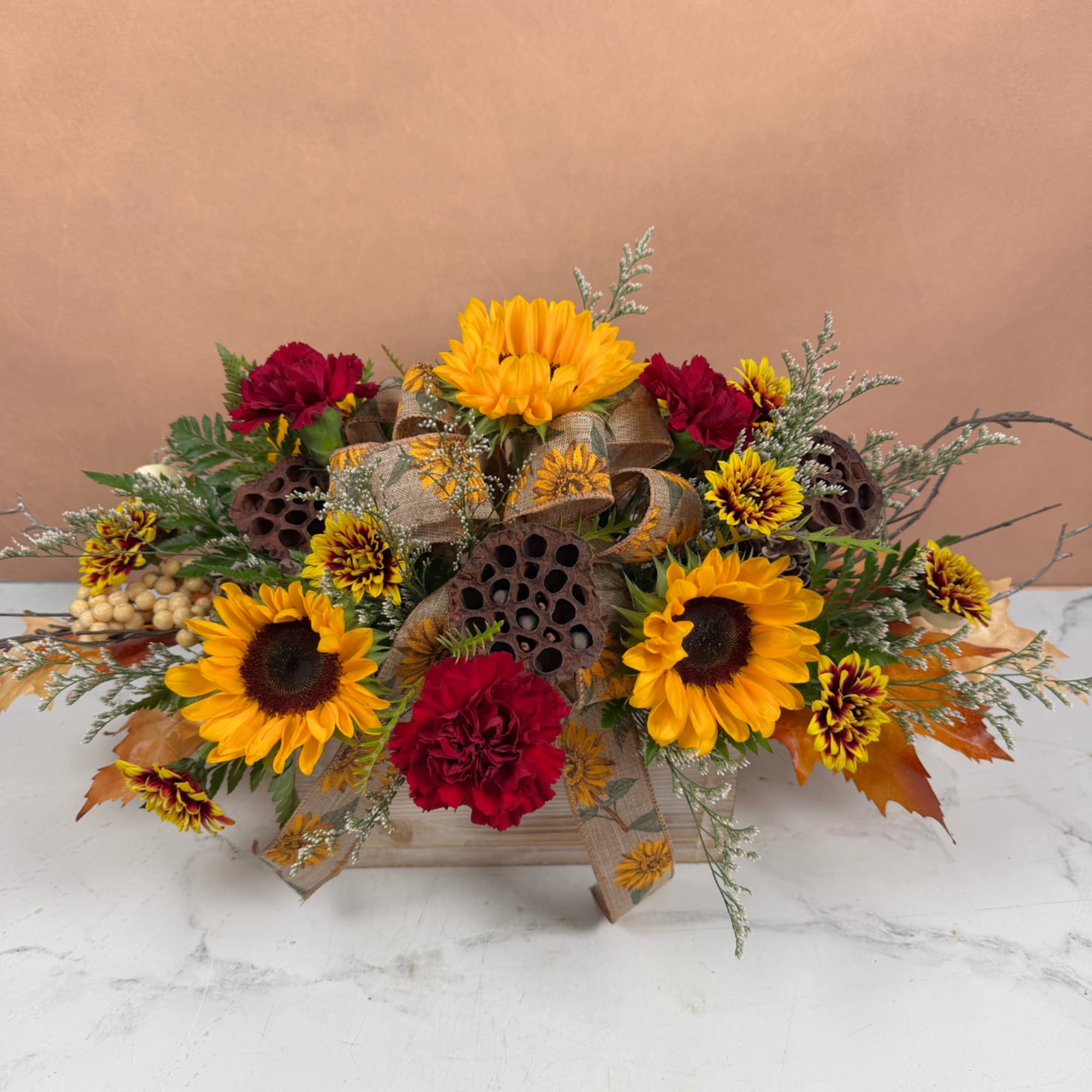 Sunflowers and red carnations in a low autumn arrangement with ribbon and decorative pods