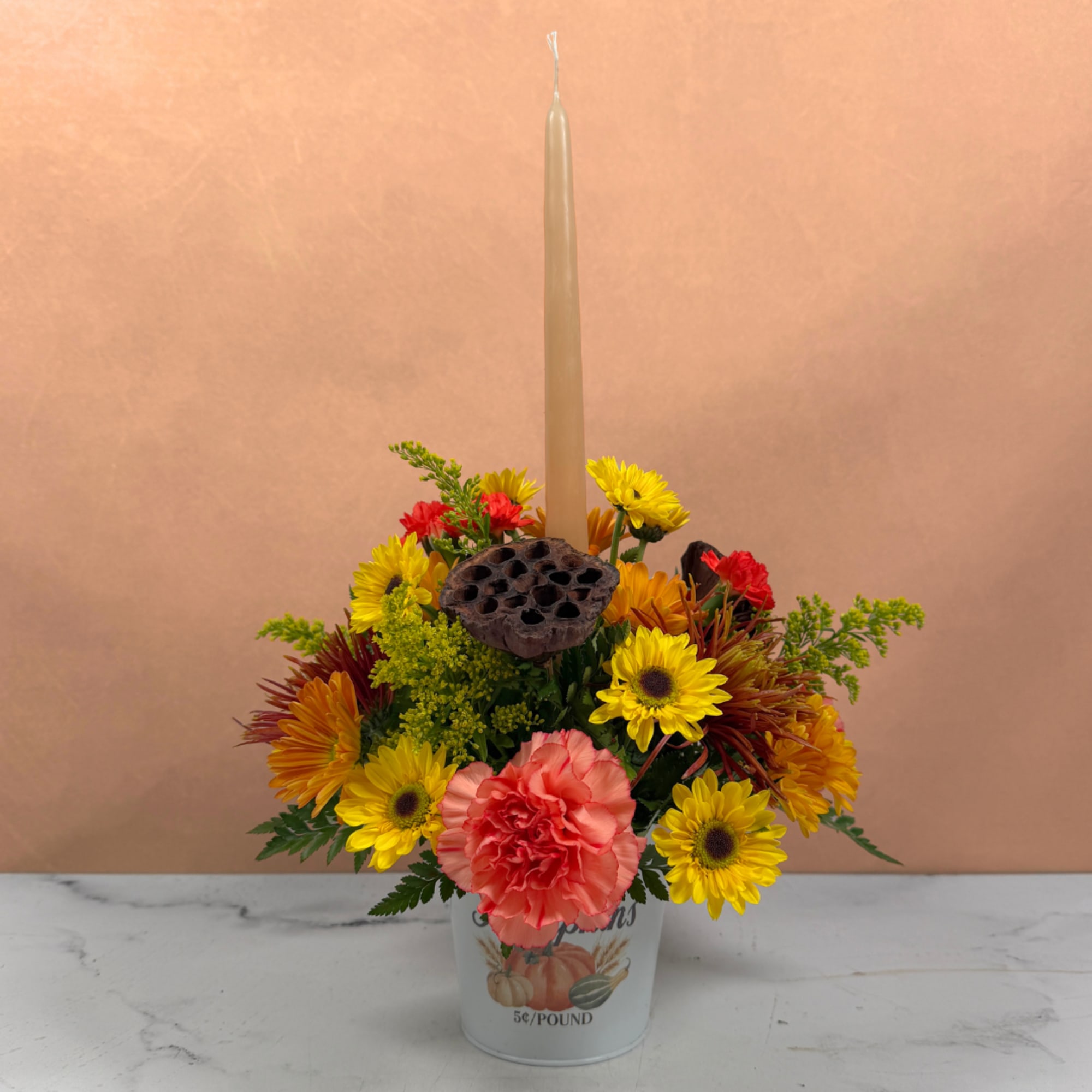 Mixed autumn flowers in a small bucket with a tall taper candle