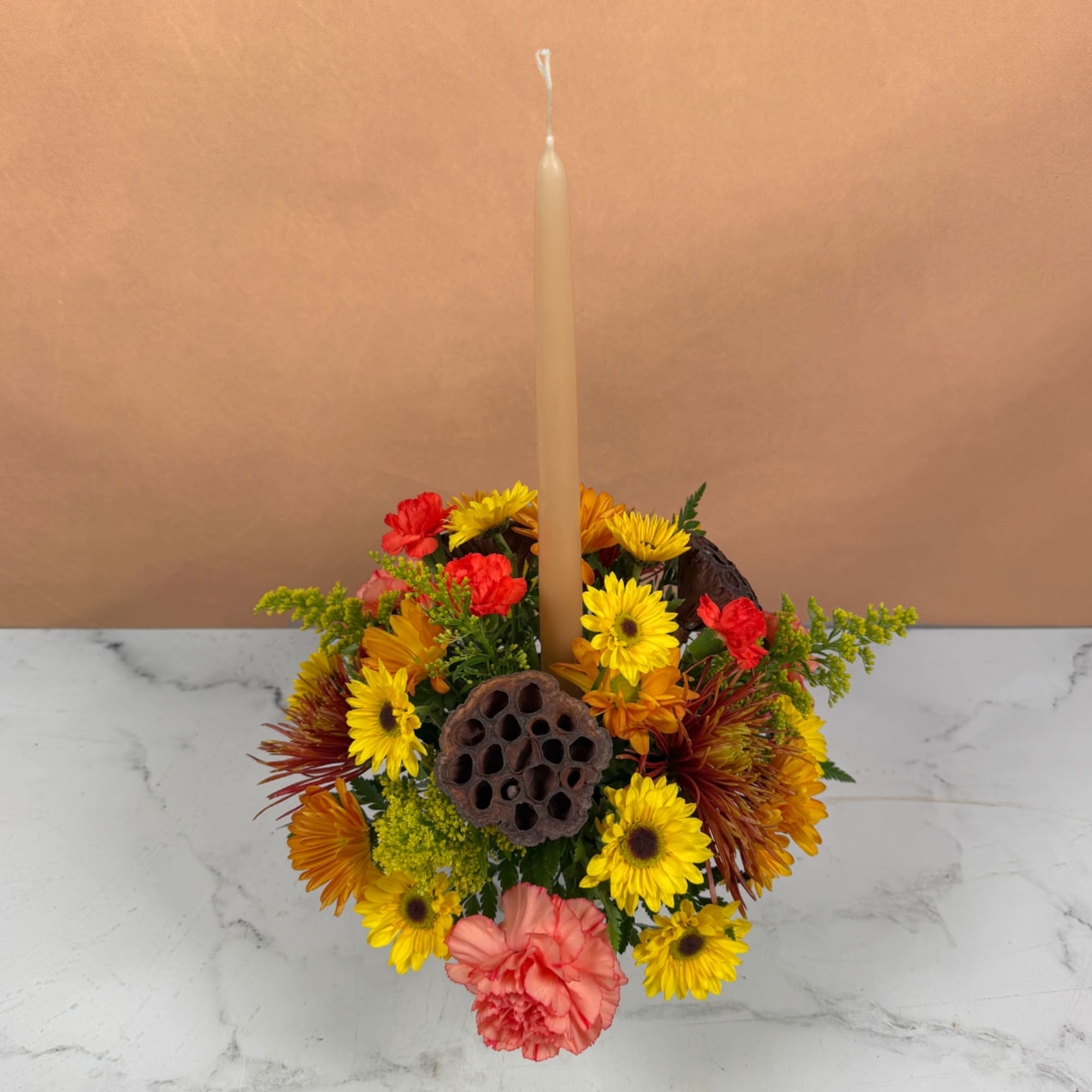 Mixed yellow, orange, and pink flowers arranged around a tall taper candle