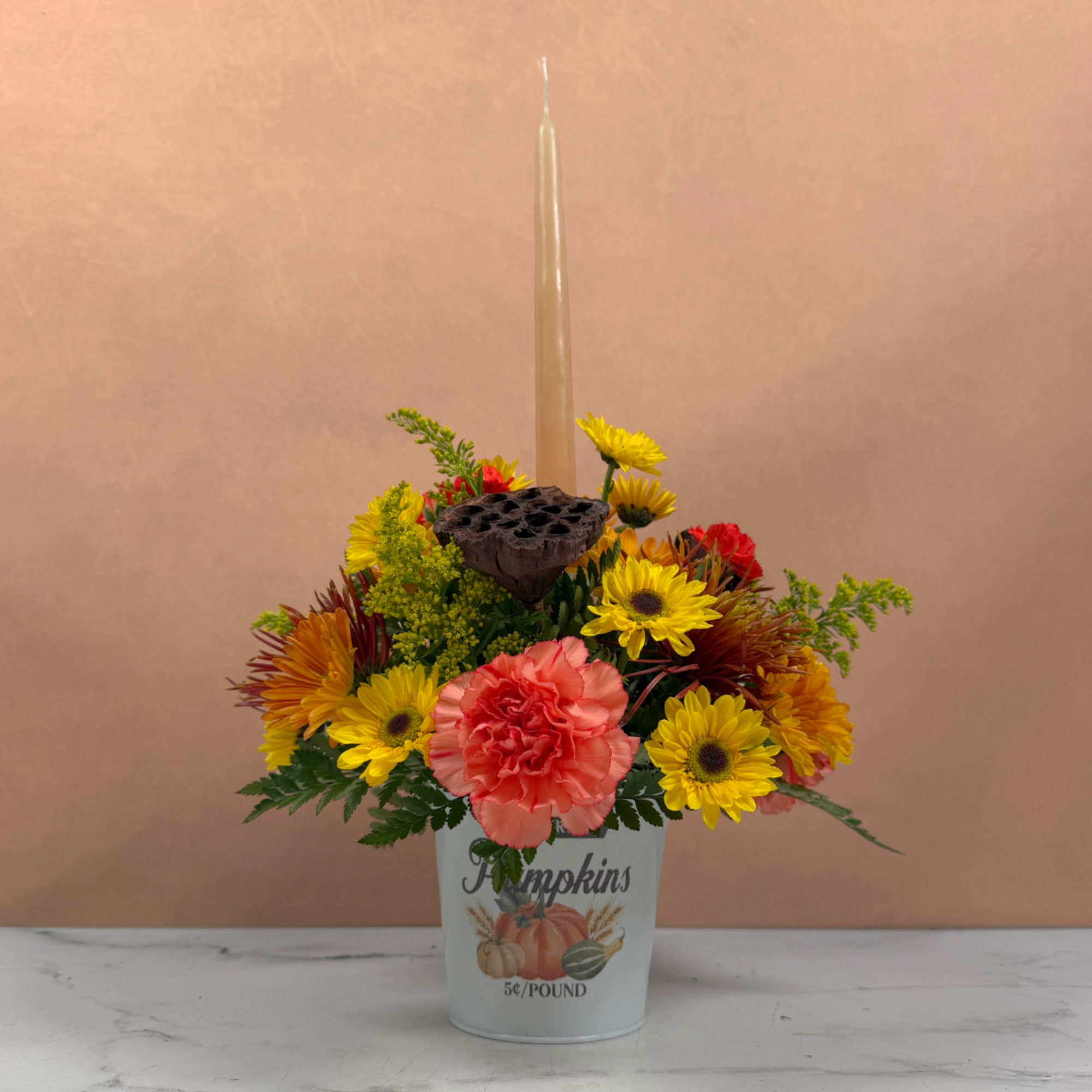 Fall flower arrangement in a pumpkin bucket with a tall candle