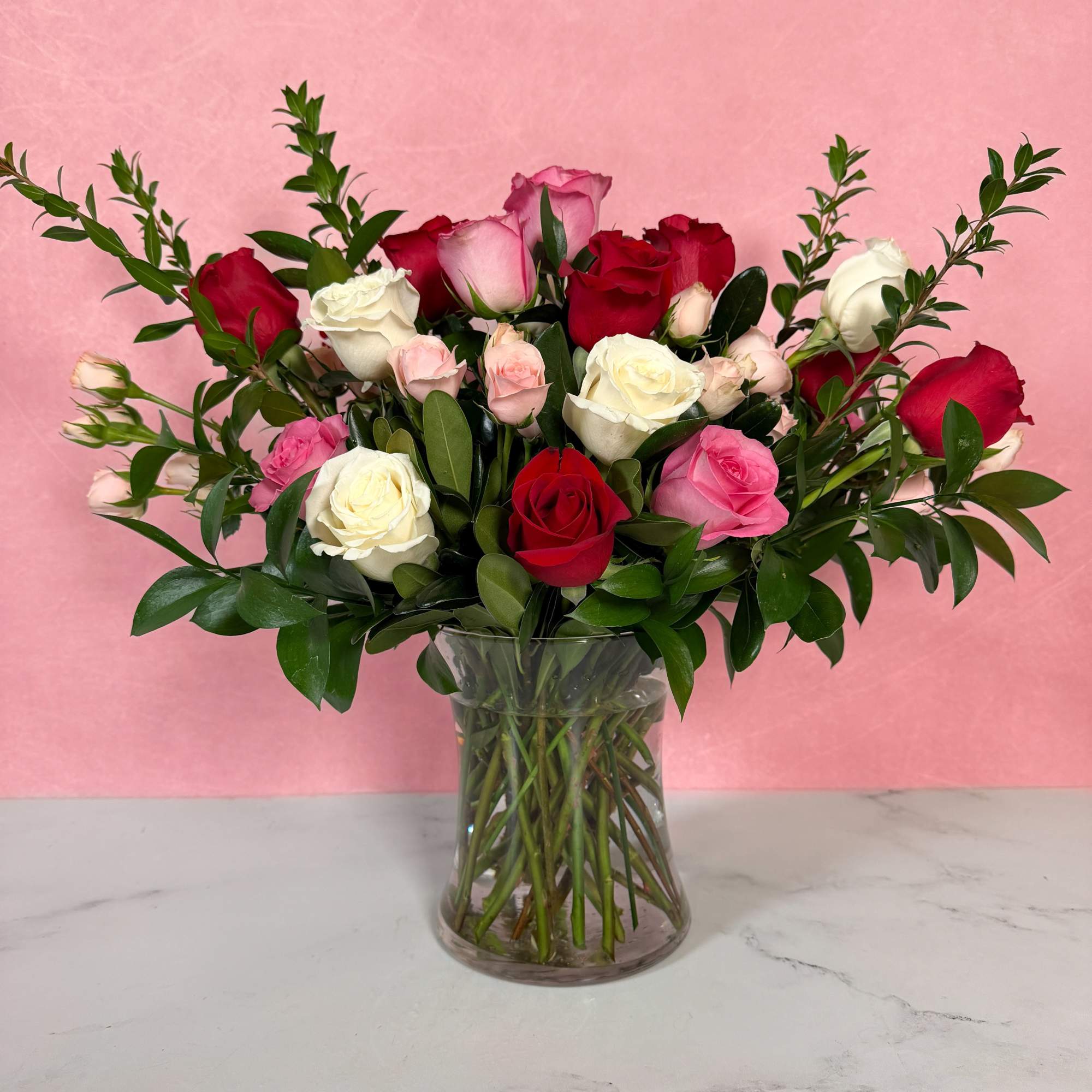 Mixed roses in a clear glass vase with greenery