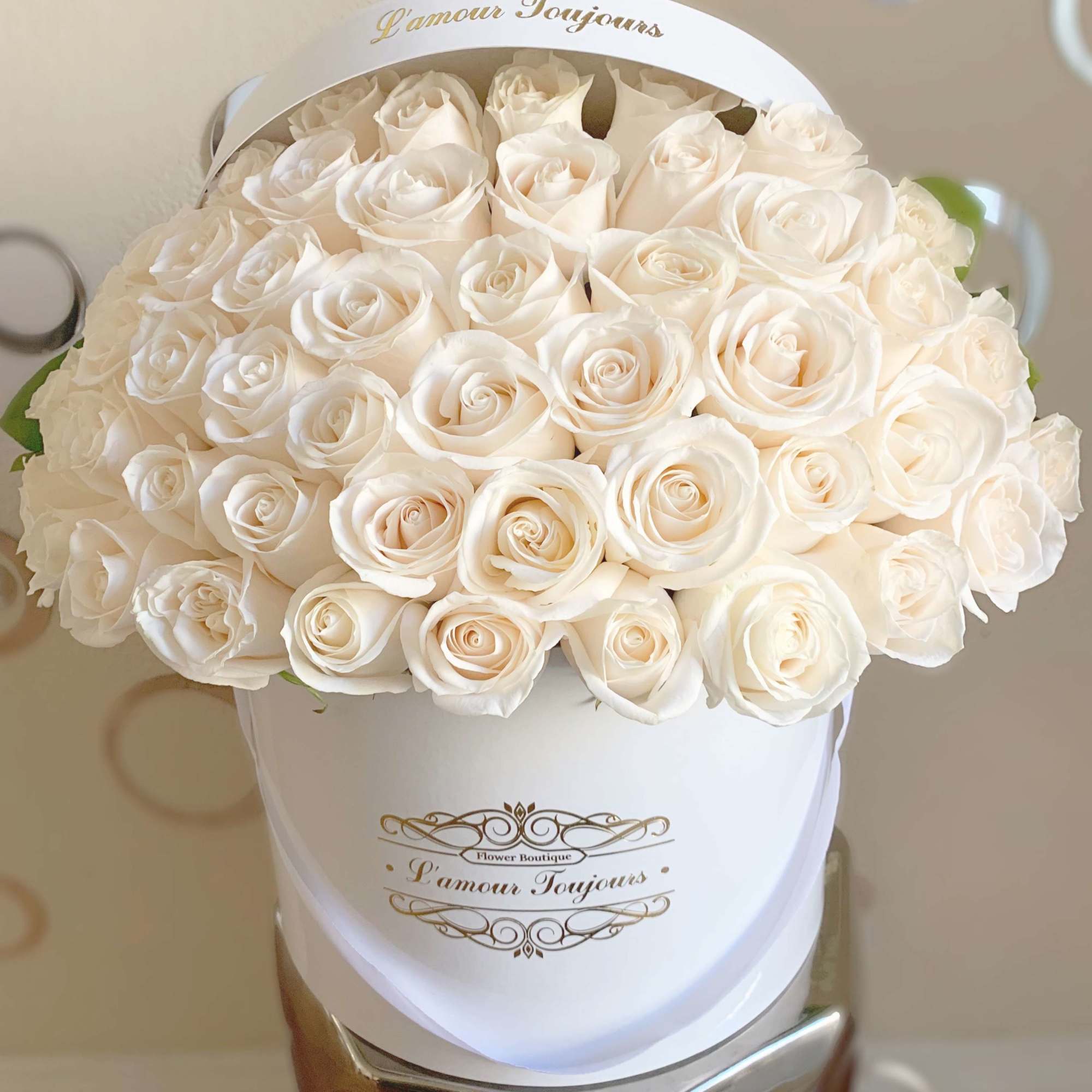 White roses arranged in a round white hat box with gold lettering