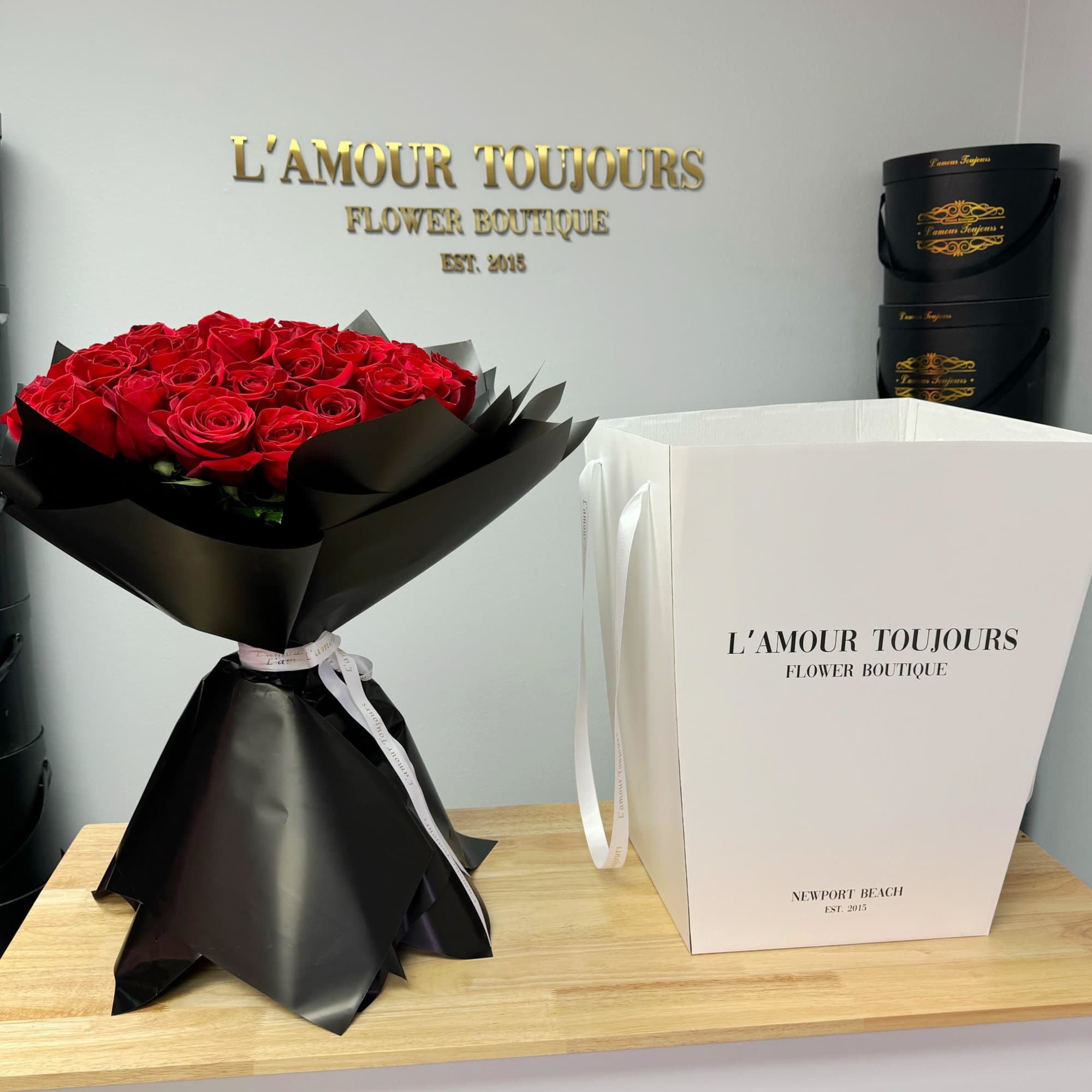 Red rose bouquet wrapped in black paper beside a white gift bag