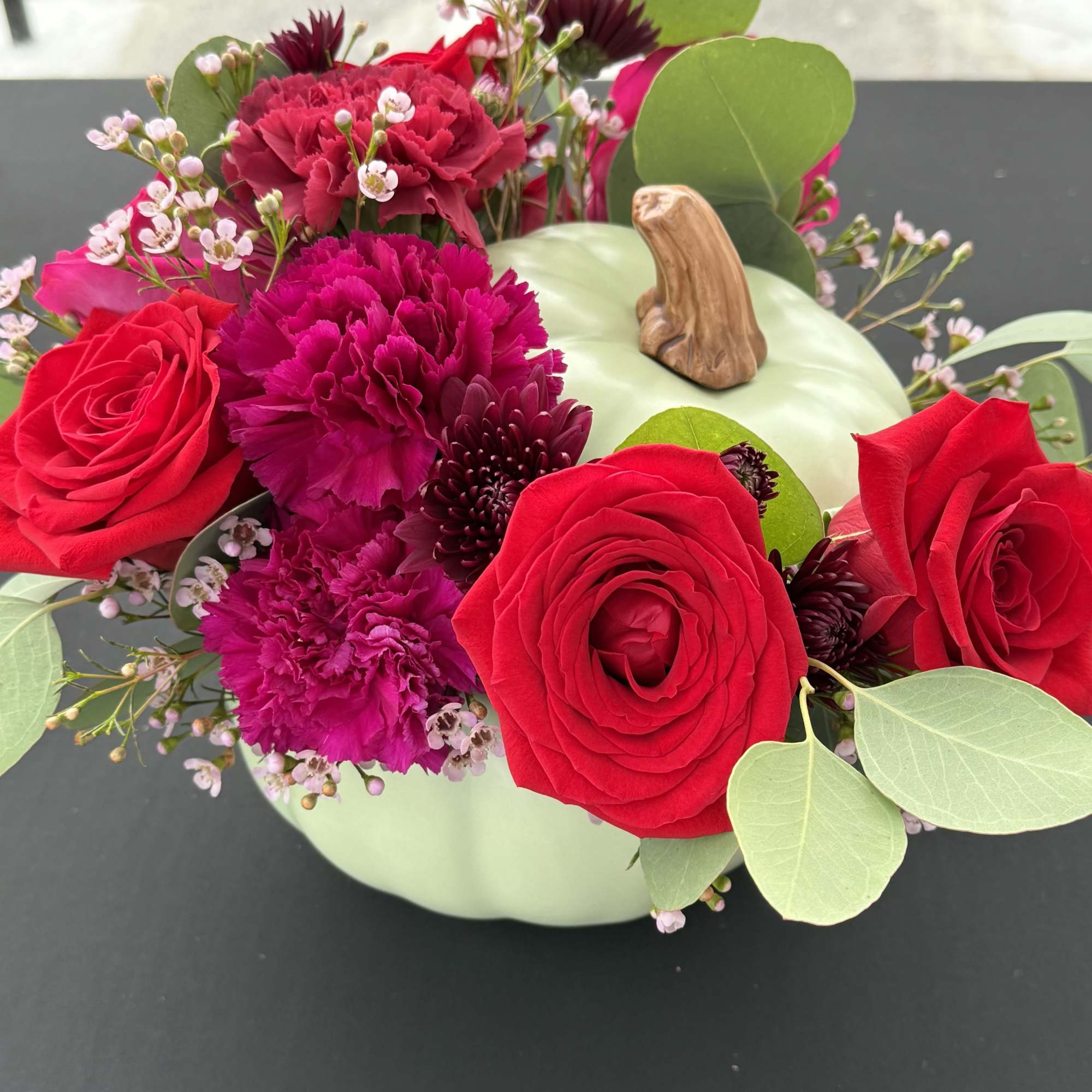 Red roses and magenta carnations arranged in a pale green pumpkin vase