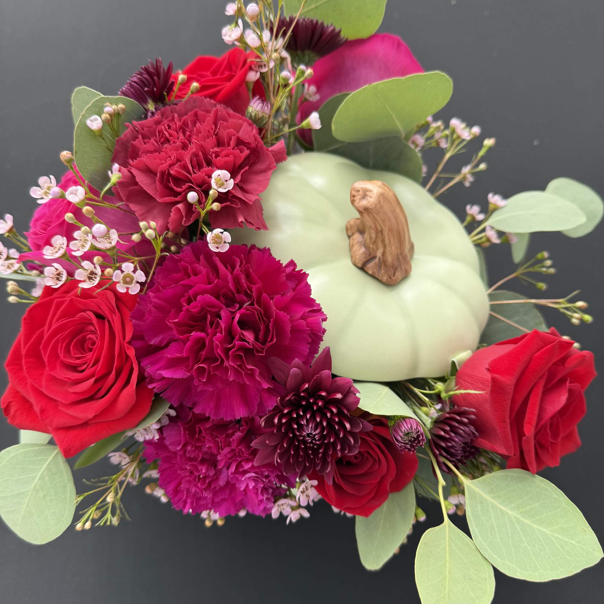 Bouquet of red roses and magenta carnations around a pale green pumpkin