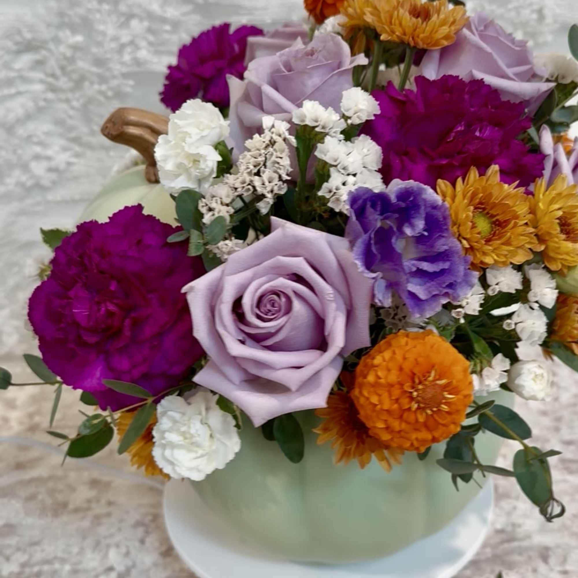 Sage ceramic pumpkin with lid filled with purple tone flowers with a