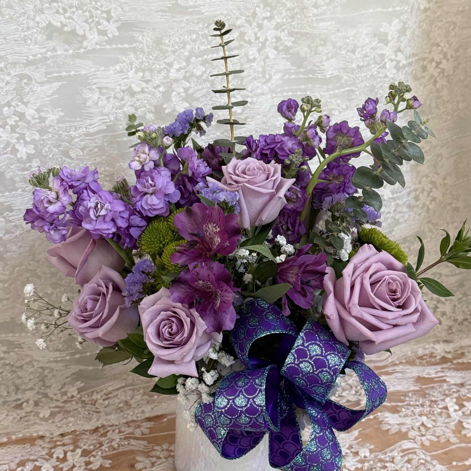 Arrangement is filled with lavender roses, lavender stock, purple alstroemeria, green mums