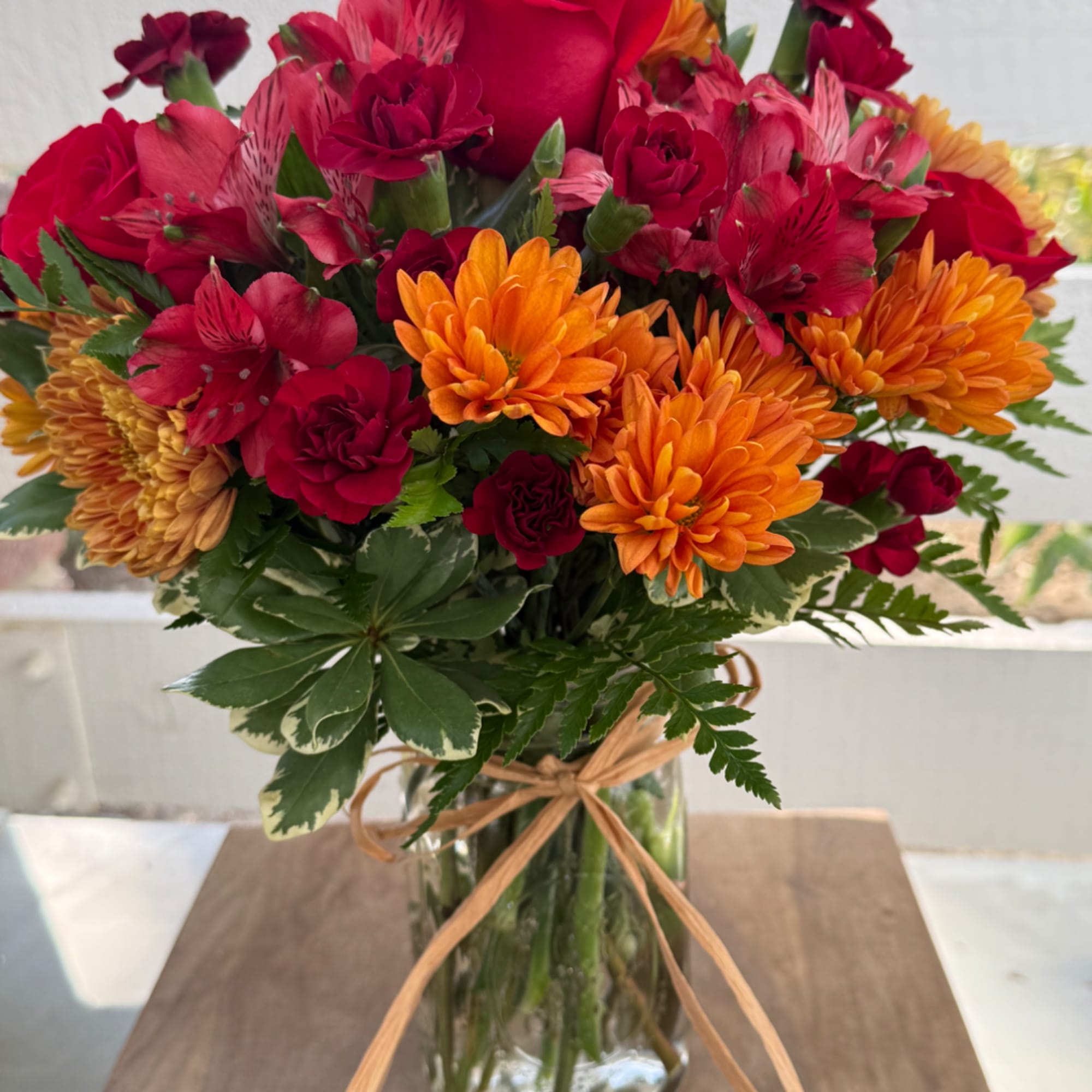 Bouquet of red and orange flowers in a glass vase with a ribbon