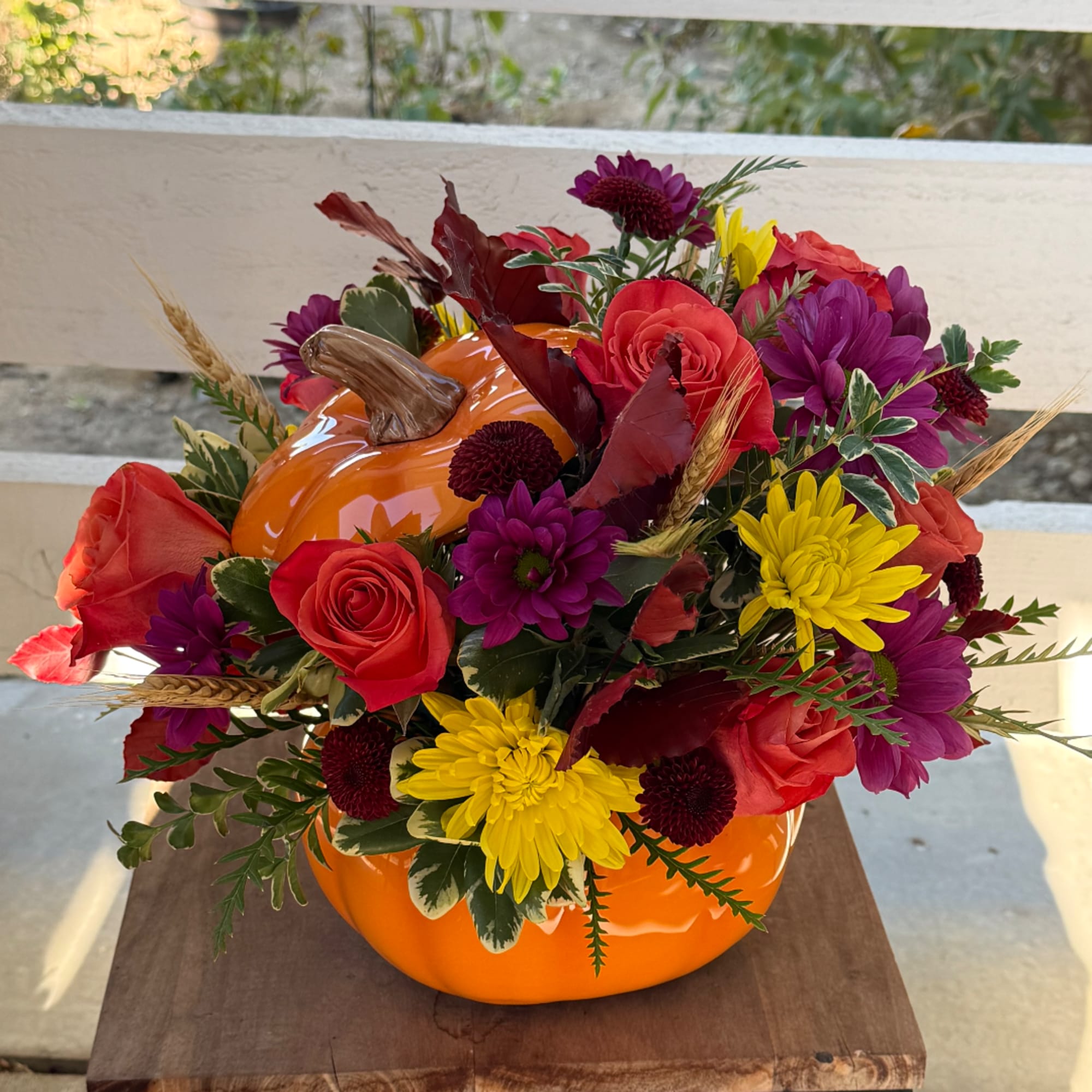 Autumn floral arrangement in an orange pumpkin container with red, purple, and yellow blooms