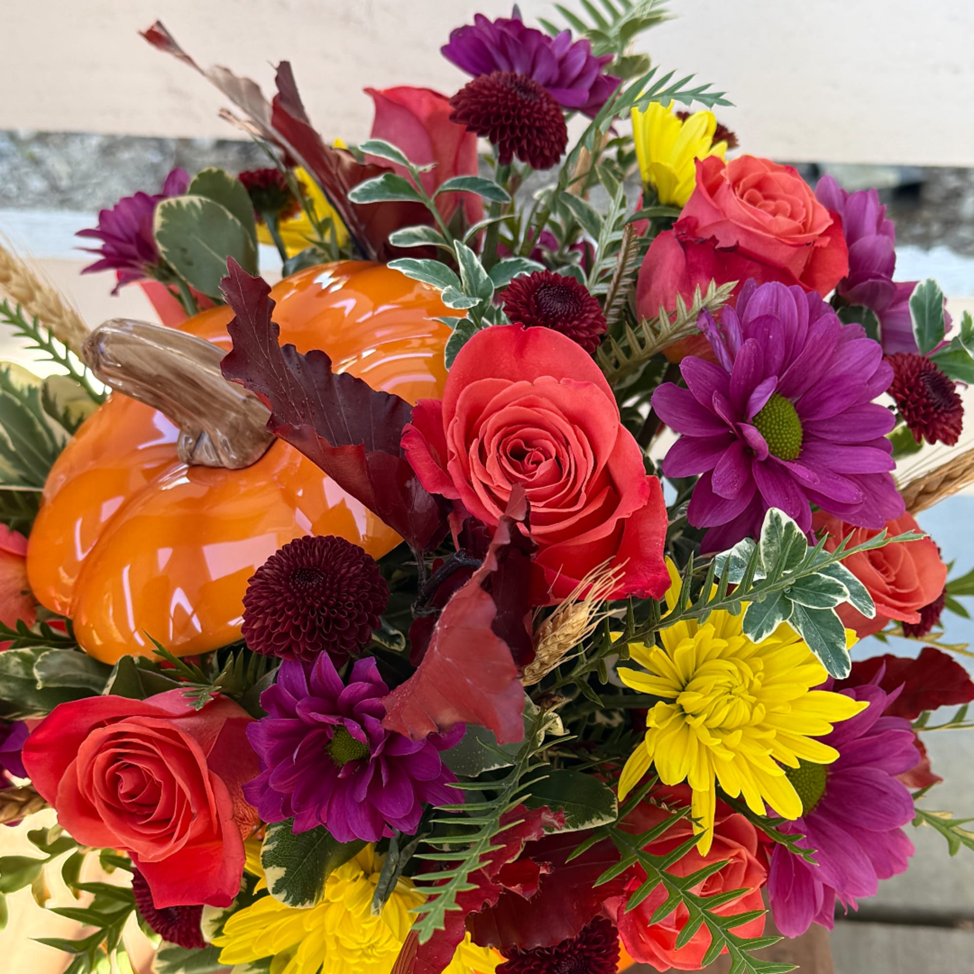 Bouquet of red roses, purple daisies, and yellow mums with an orange pumpkin accent