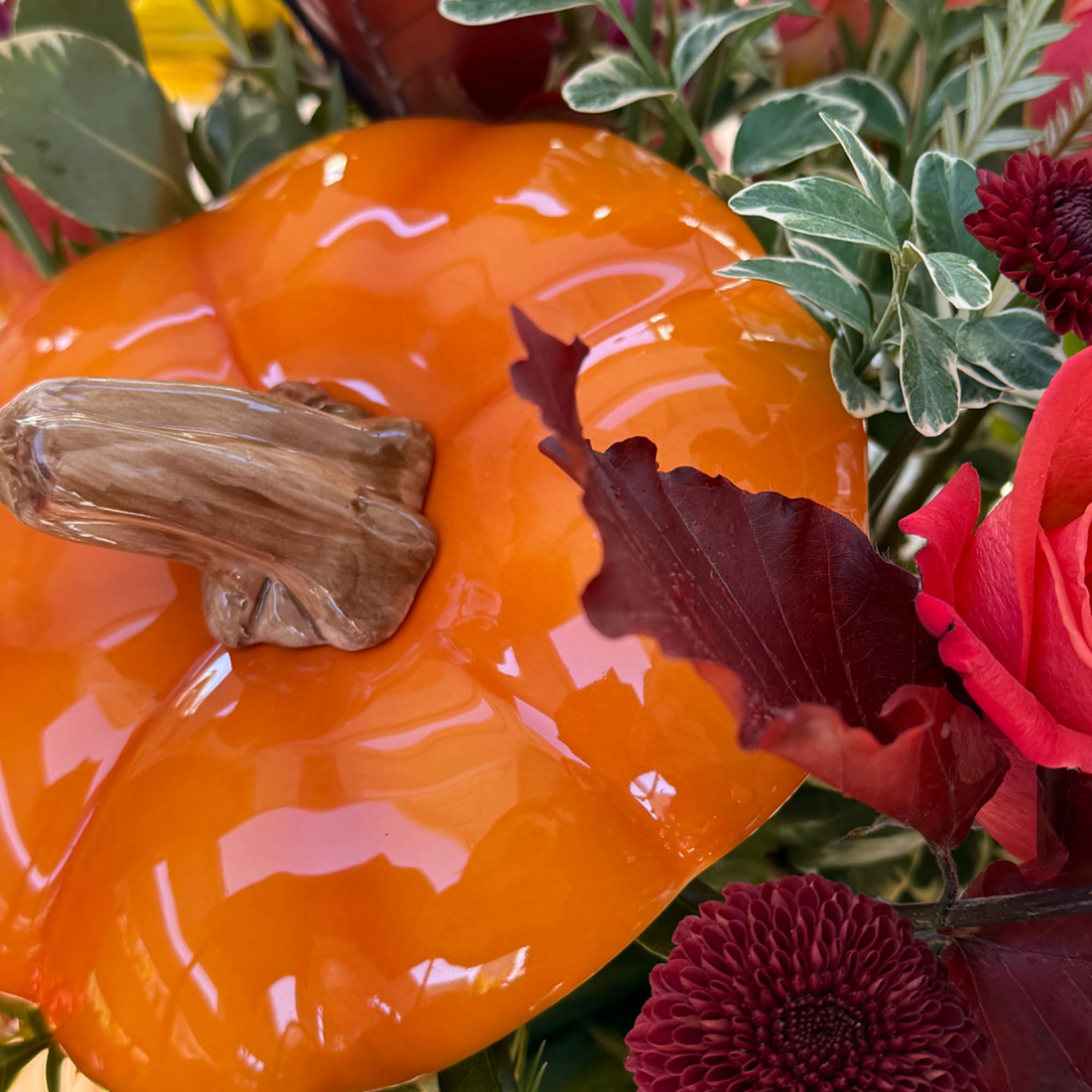Orange pumpkin centerpiece with red flowers and variegated foliage