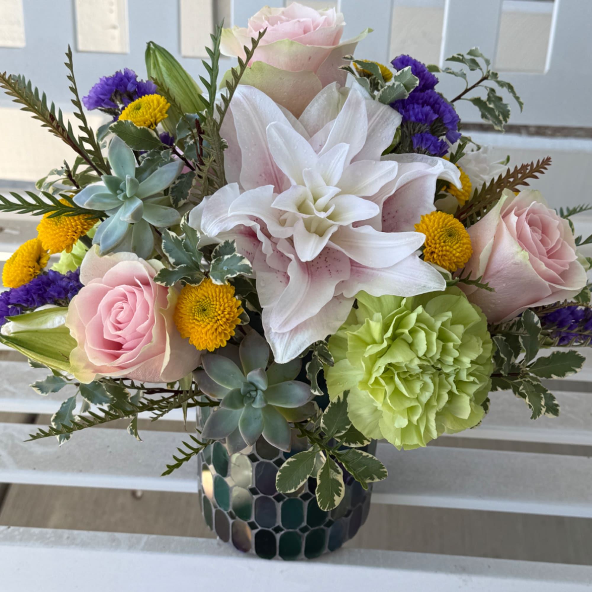 Mixed bouquet in a dark mosaic vase with pink roses, white lilies, and yellow blooms