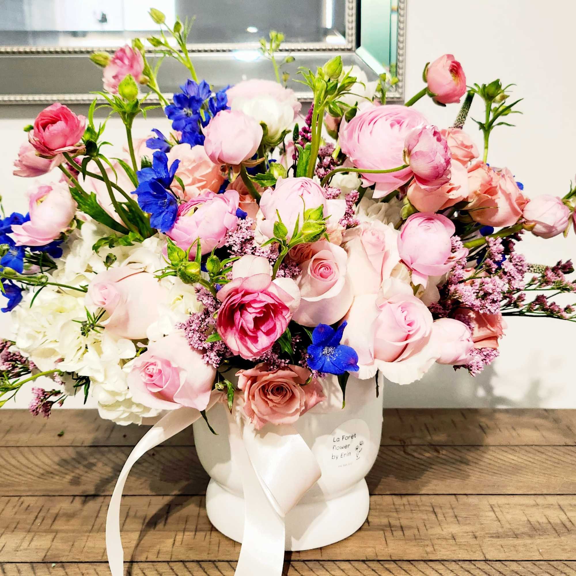 Pink and blue mixed flower arrangement in a white vase with ribbon