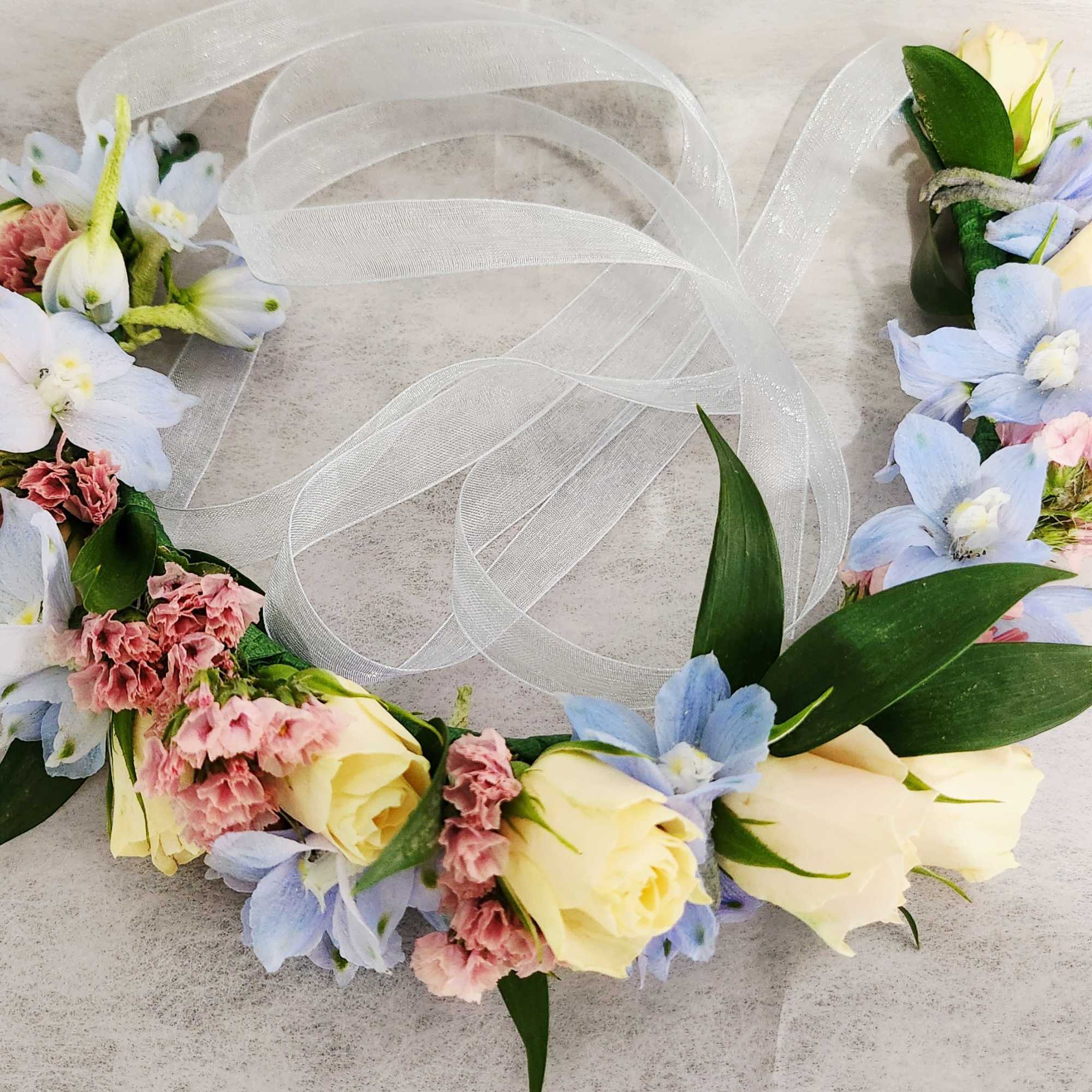 Floral crown with pale roses, blue flowers, and white ribbon
