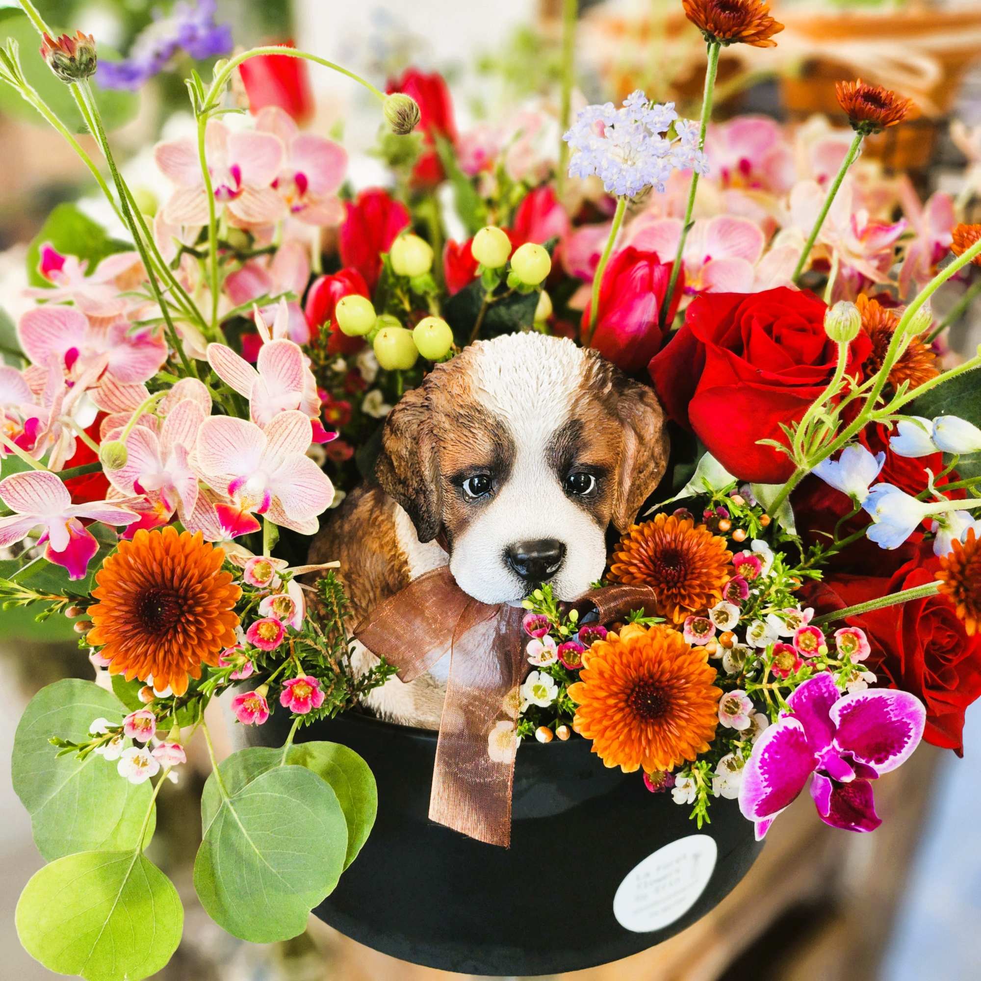 Flower arrangement in a black hatbox with a puppy figurine