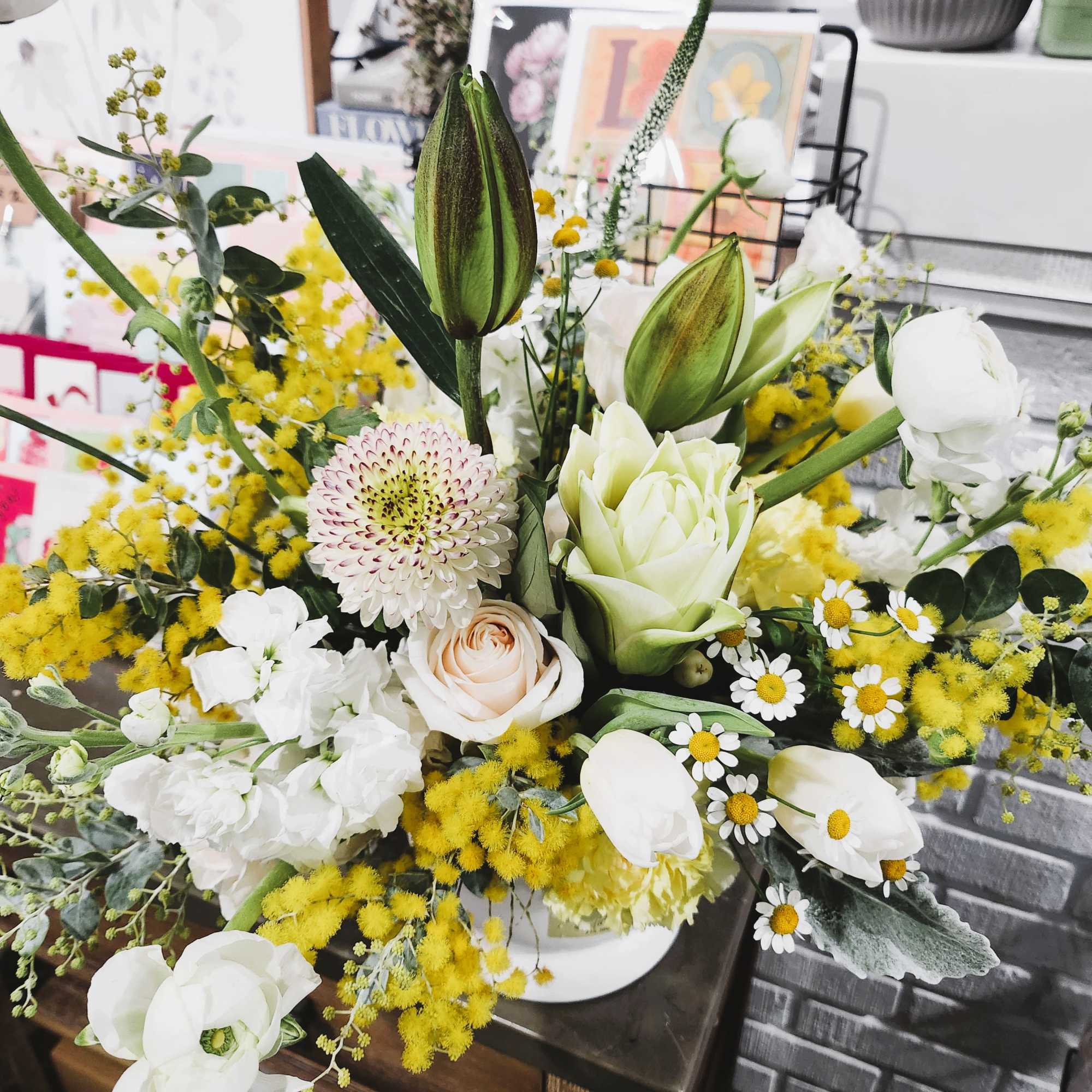 Mixed bouquet with white lilies, roses, and yellow filler flowers in a white vase