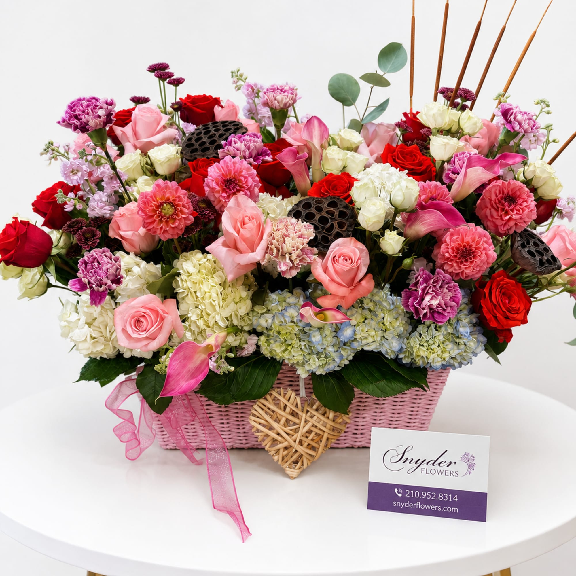 Pink and red mixed flower arrangement in a pink basket with ribbon