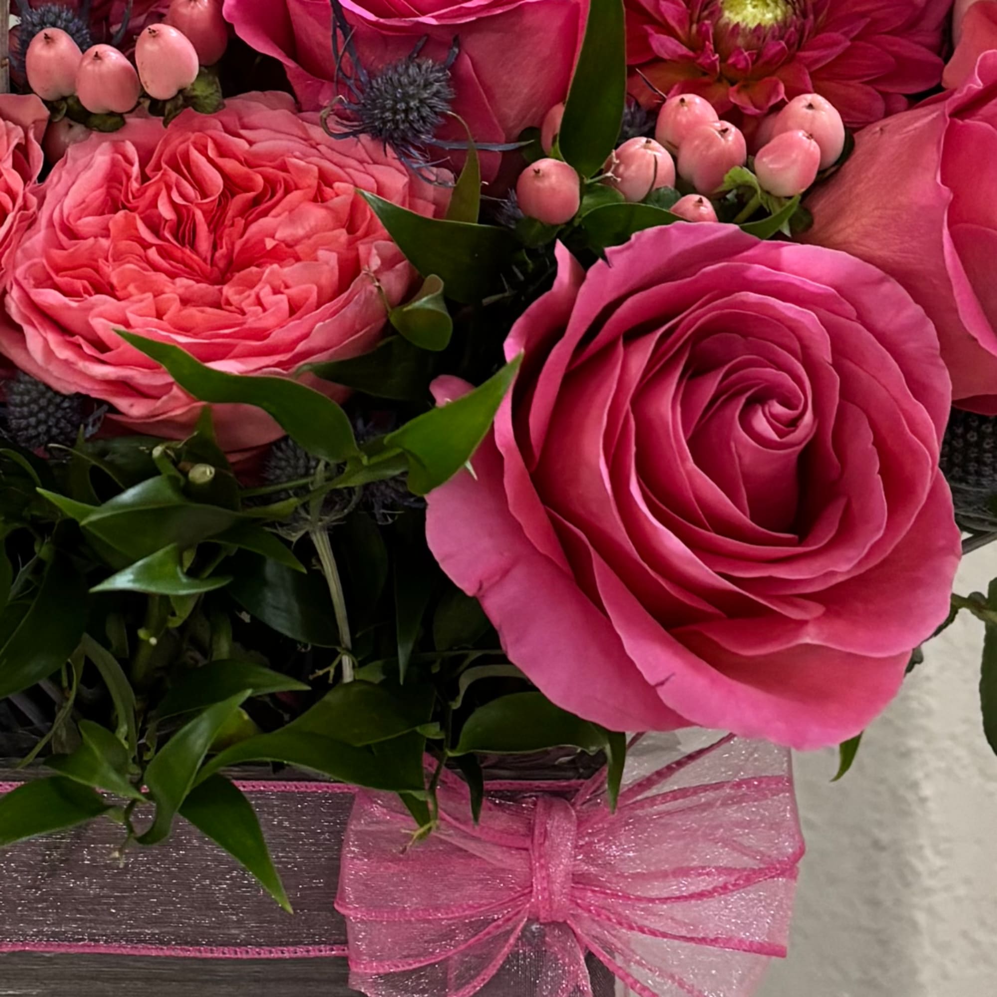 Pink roses arranged in a box with green foliage and a pink ribbon