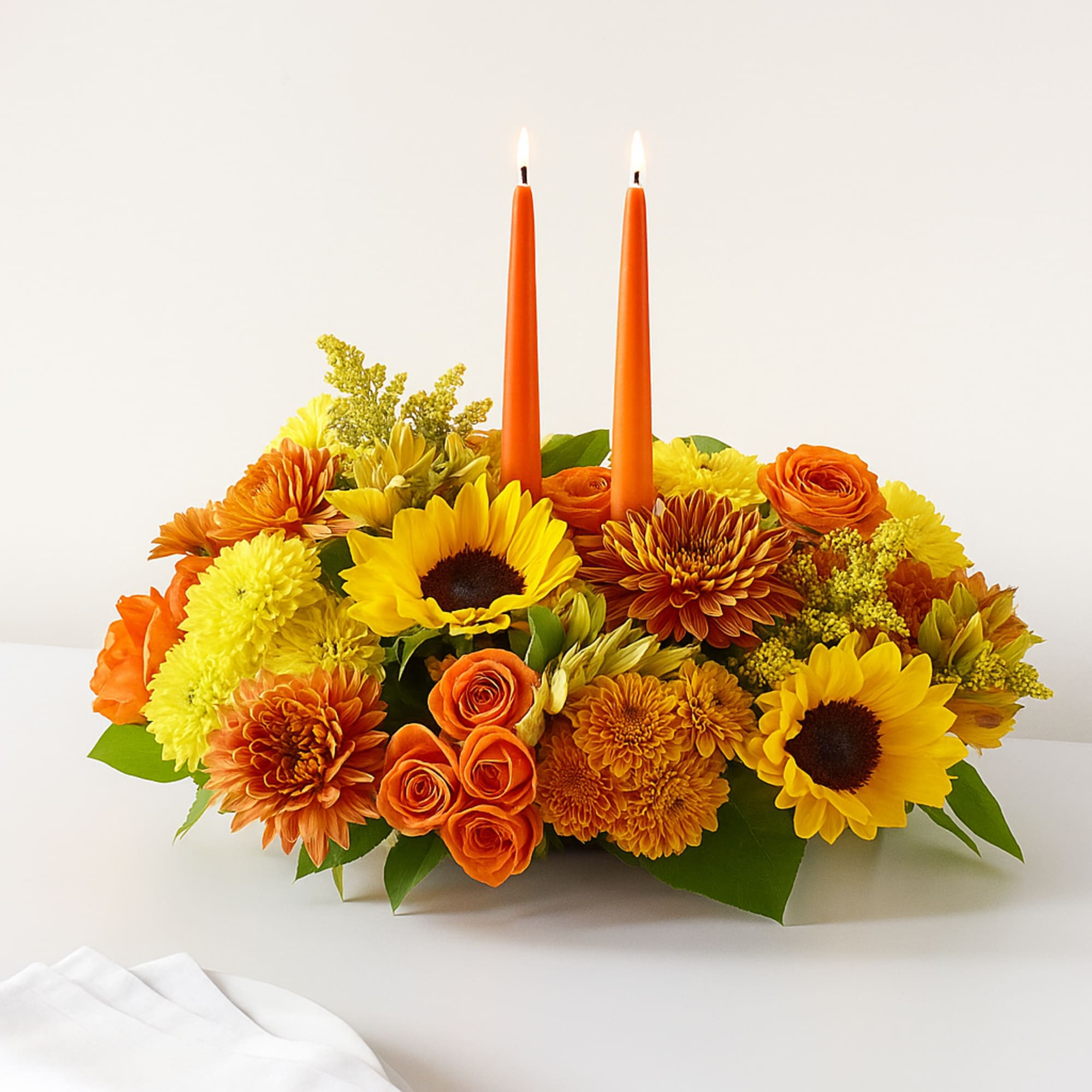 Orange and yellow floral centerpiece with two lit orange candles