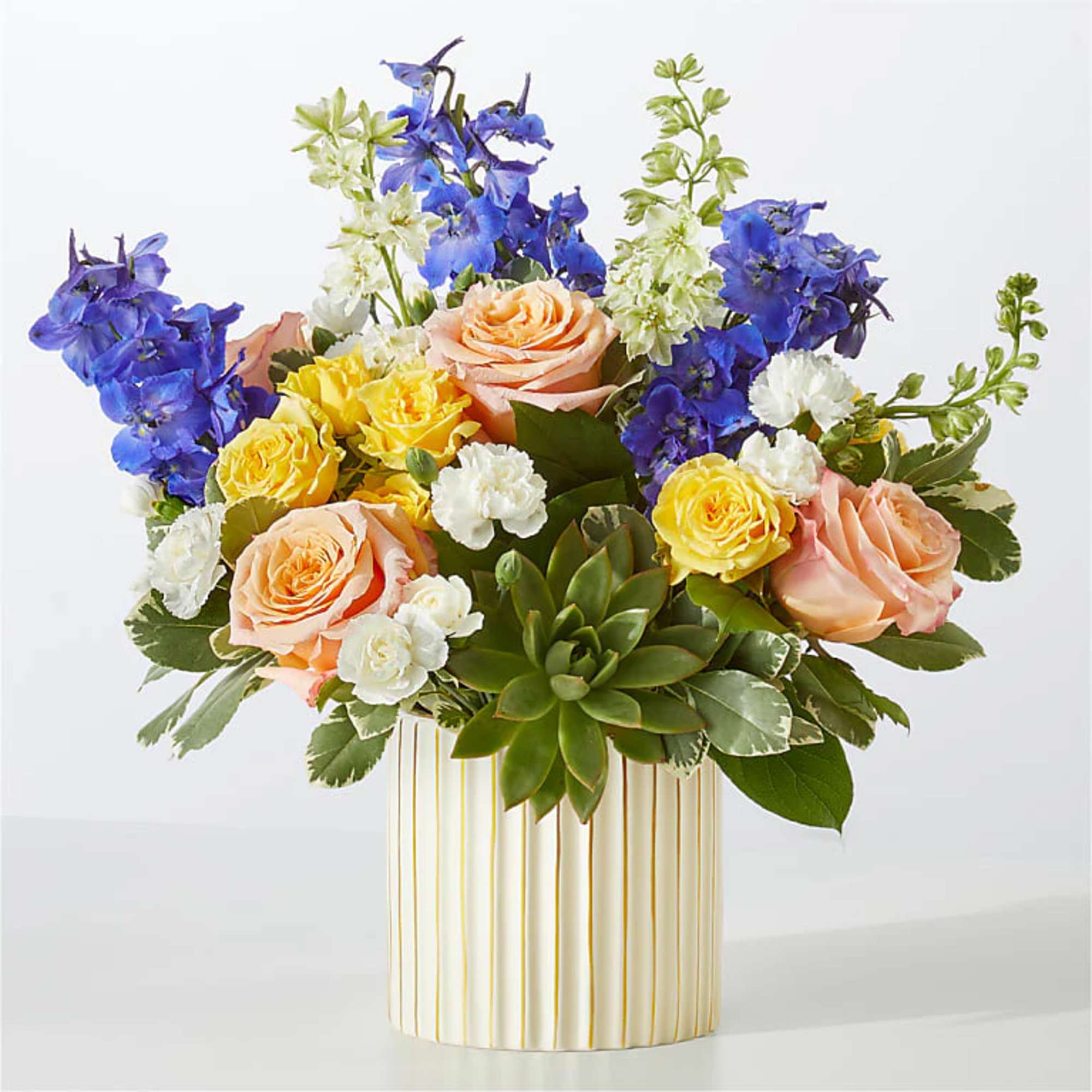 Mixed bouquet of roses, blue delphinium, and white carnations in a striped vase