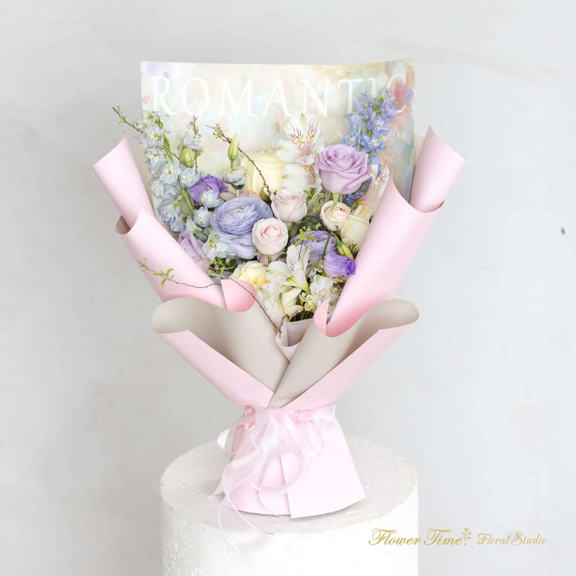 Pastel bouquet of roses, lilies, and blue flowers wrapped in pink paper